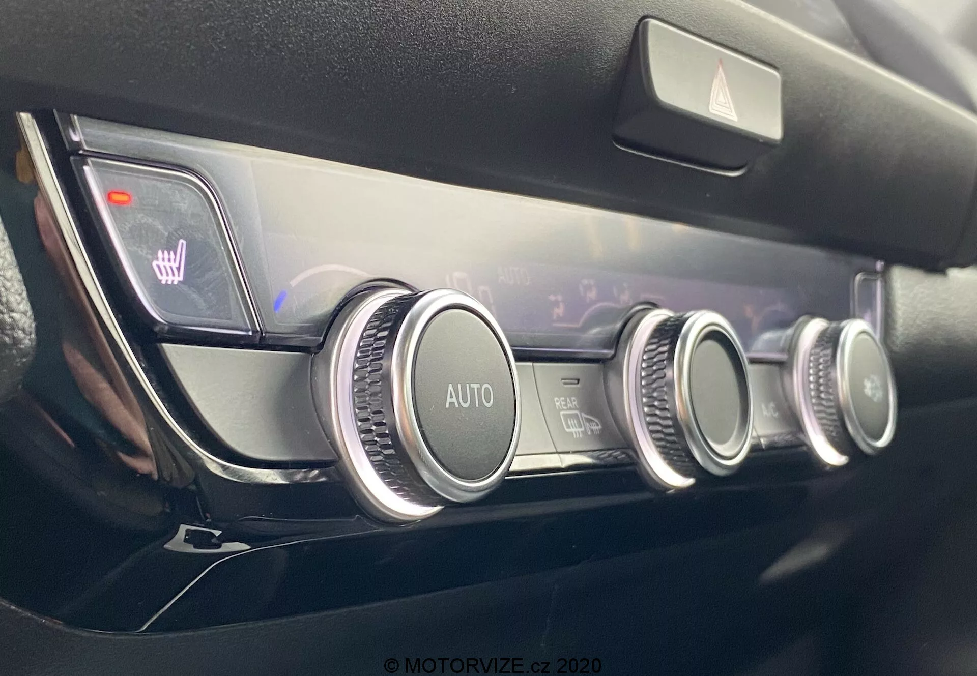 Vista de cerca del moderno panel de control climático del Honda Jazz 2020, que cuenta con tres diales circulares con acabado metálico, un sistema de control climático automático, configuraciones de temperatura de doble zona indicadas en una pantalla digital, e iconos iluminados de asientos calefactados, todo en un diseño minimalista y de alta calidad del tablero de instrumentos.