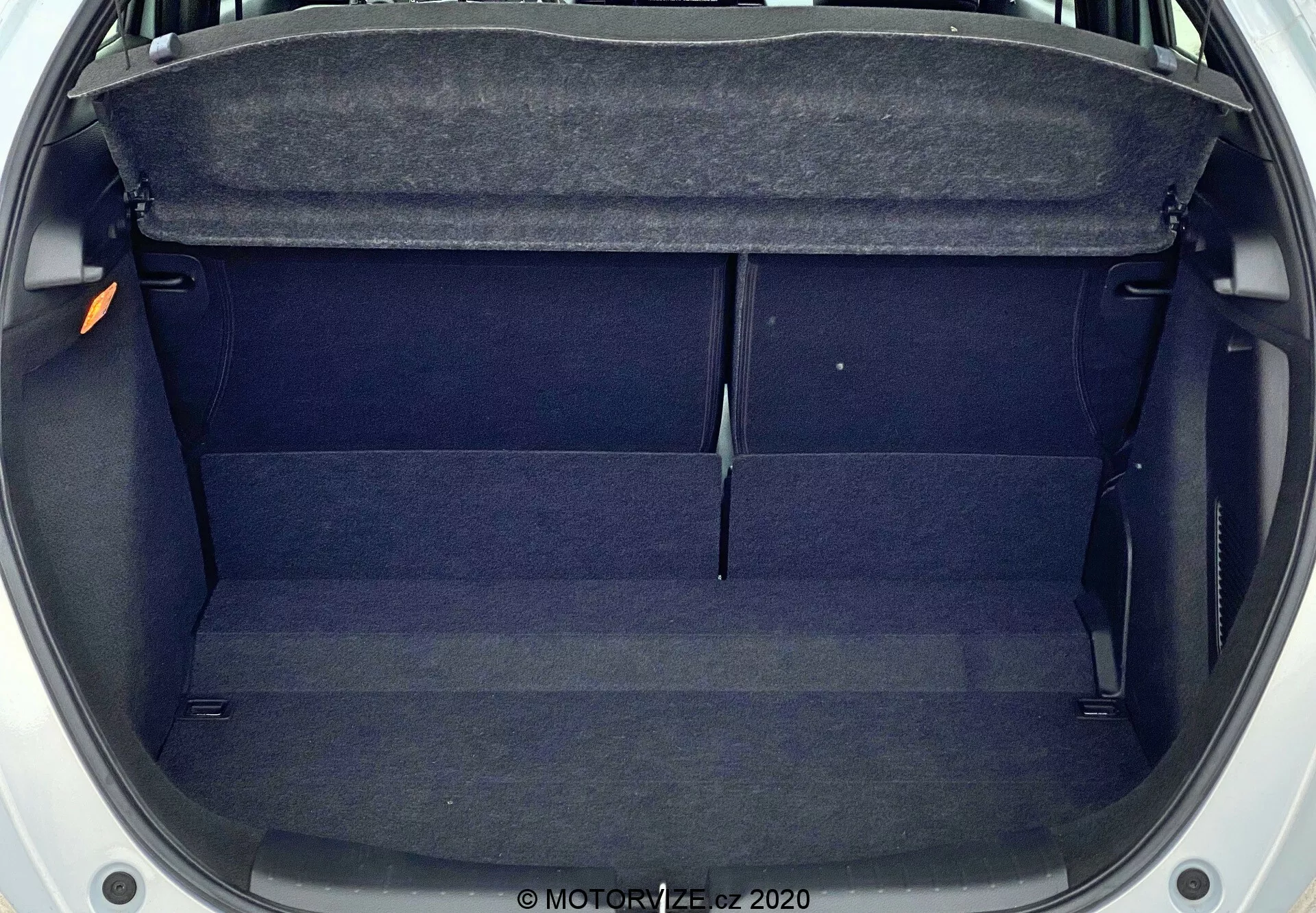 Vista aérea del maletero vacío del Honda Jazz 2020, mostrando un espacio rectangular de tamaño moderado con revestimiento de tela oscura. Las características incluyen un estante en la parte superior, molduras interiores a los lados y una ligera elevación en el centro. El maletero está limpio, sin obstrucciones y parece bien mantenido.