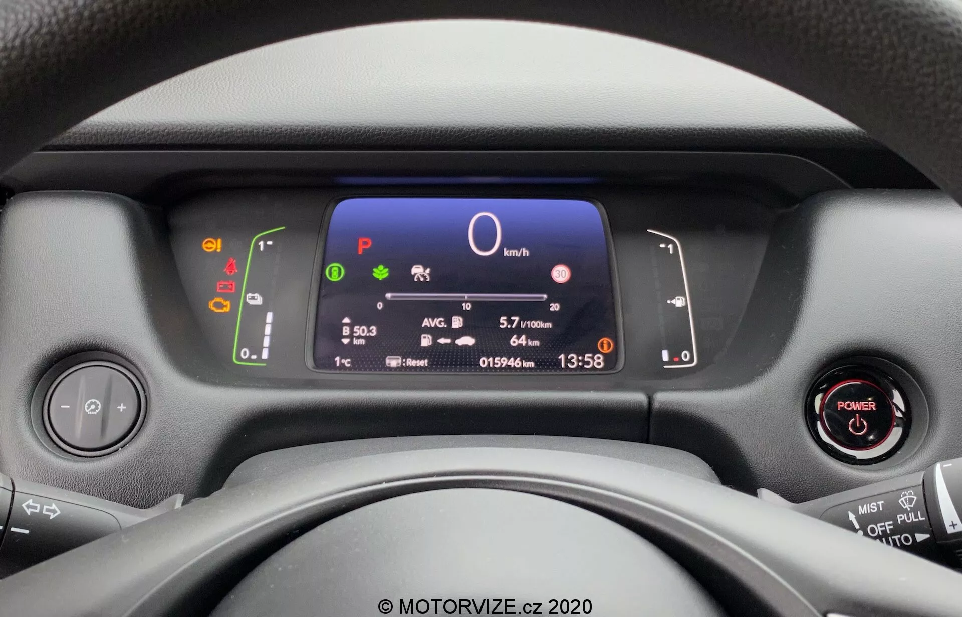 Vista desde el asiento del conductor de un Honda Jazz 2020, enfocada en el moderno cuadro de instrumentos, volante y controles del tablero. La pantalla digital muestra información clave del vehículo, incluyendo velocidad, selección de marcha, eficiencia de combustible, hora y temperatura, con encendido sin llave y controles multifuncionales en el volante visibles.