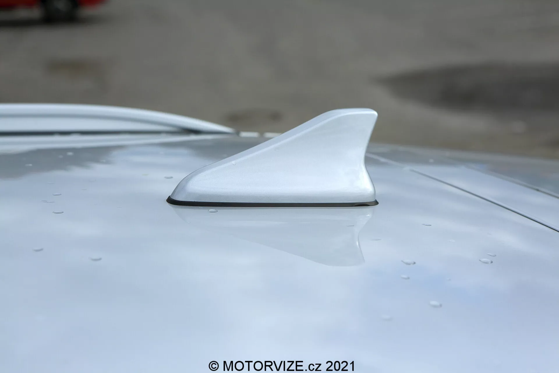 Primer plano de la antena tipo aleta de tiburón en el techo de un Hyundai i30 2020 blanco, mostrando su diseño aerodinámico desde un ángulo lateral y ligeramente elevado con enfoque en la integración suave y gotas visibles que indican lluvia reciente o lavado.