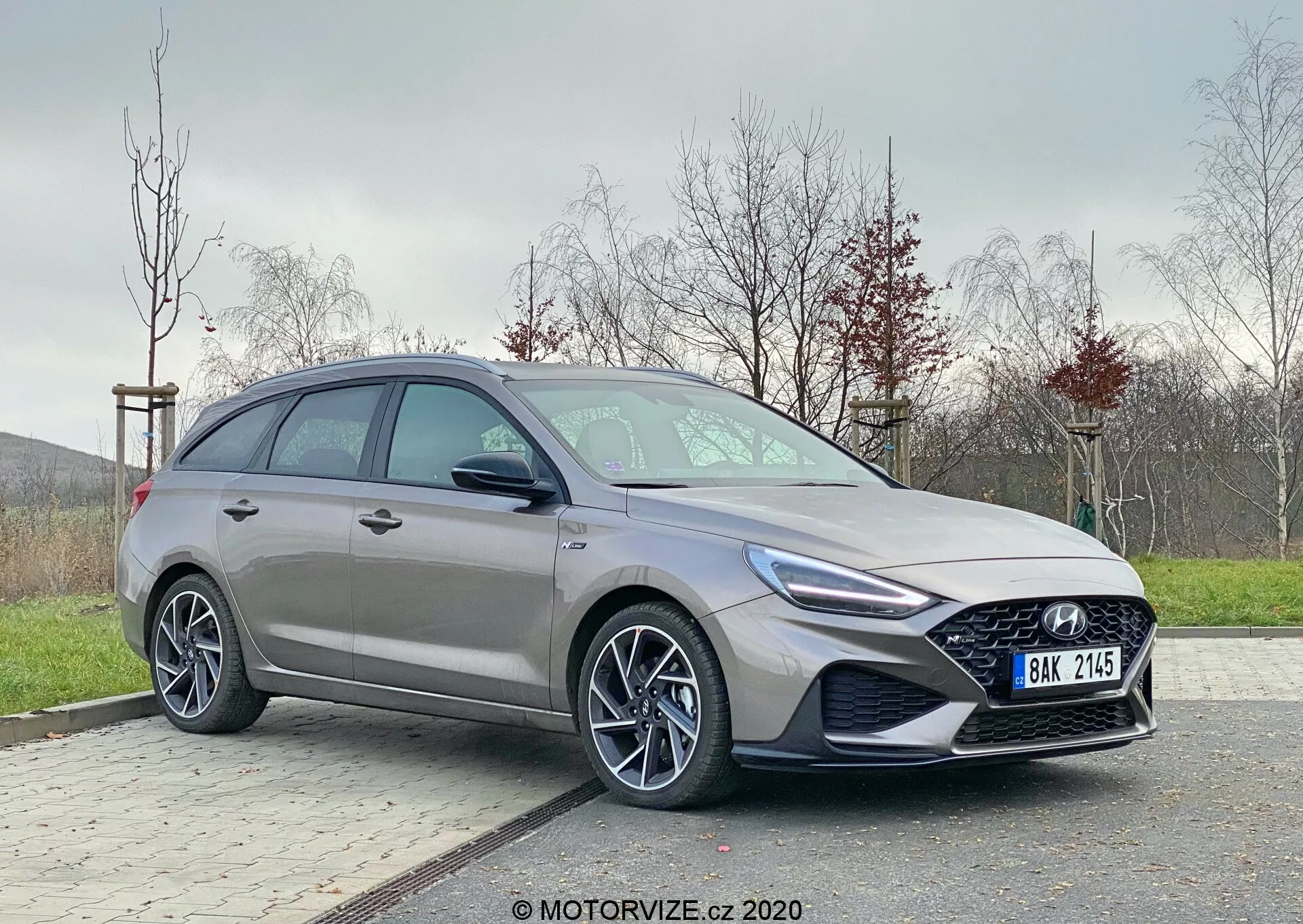 Hyundai i30 2020 moderno visto desde un ángulo frontal de tres cuartos. Se enfoca en el lado del conductor mostrando detalles de diseño elegantes como faros agresivos con luces diurnas LED, parrilla prominente, llantas de aleación de varios radios y perfil lateral contorneado. Posicionado fuera del centro en un área pavimentada con fondo de césped, mostrando un hatchback moderno y dinámico con tecnologías automotrices avanzadas.