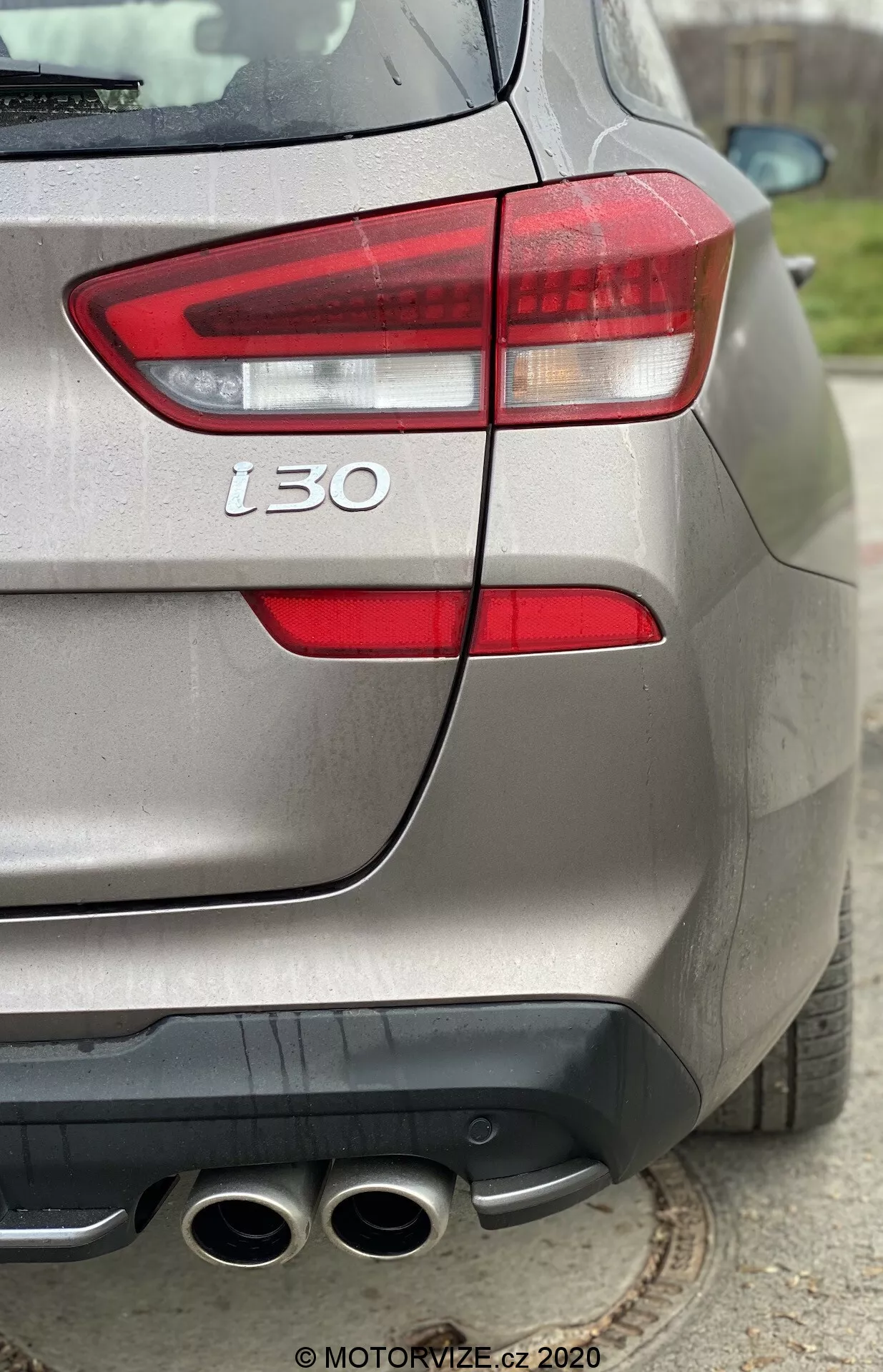 Vista en primer plano de tres cuartos traseros de un Hyundai i30 2020 plateado, destacando su luz trasera izquierda, parachoques trasero, escape de cuatro salidas, insignia 't30' y acabado de pintura metálica, destacando los detalles de diseño y rendimiento del vehículo.