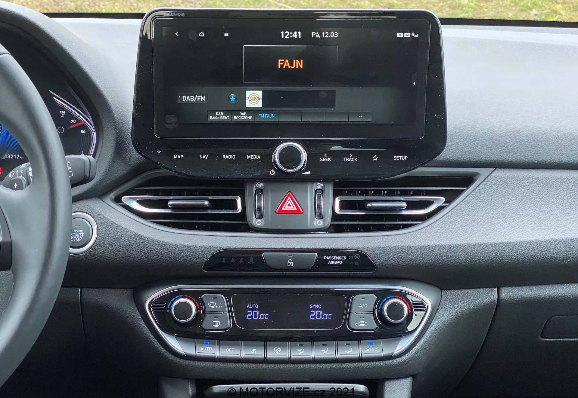 Consola central del Hyundai i30 2020 que muestra un moderno sistema de infoentretenimiento con pantalla táctil, interfaz de radio, control de clima de doble zona y respiraderos con acabado metálico.