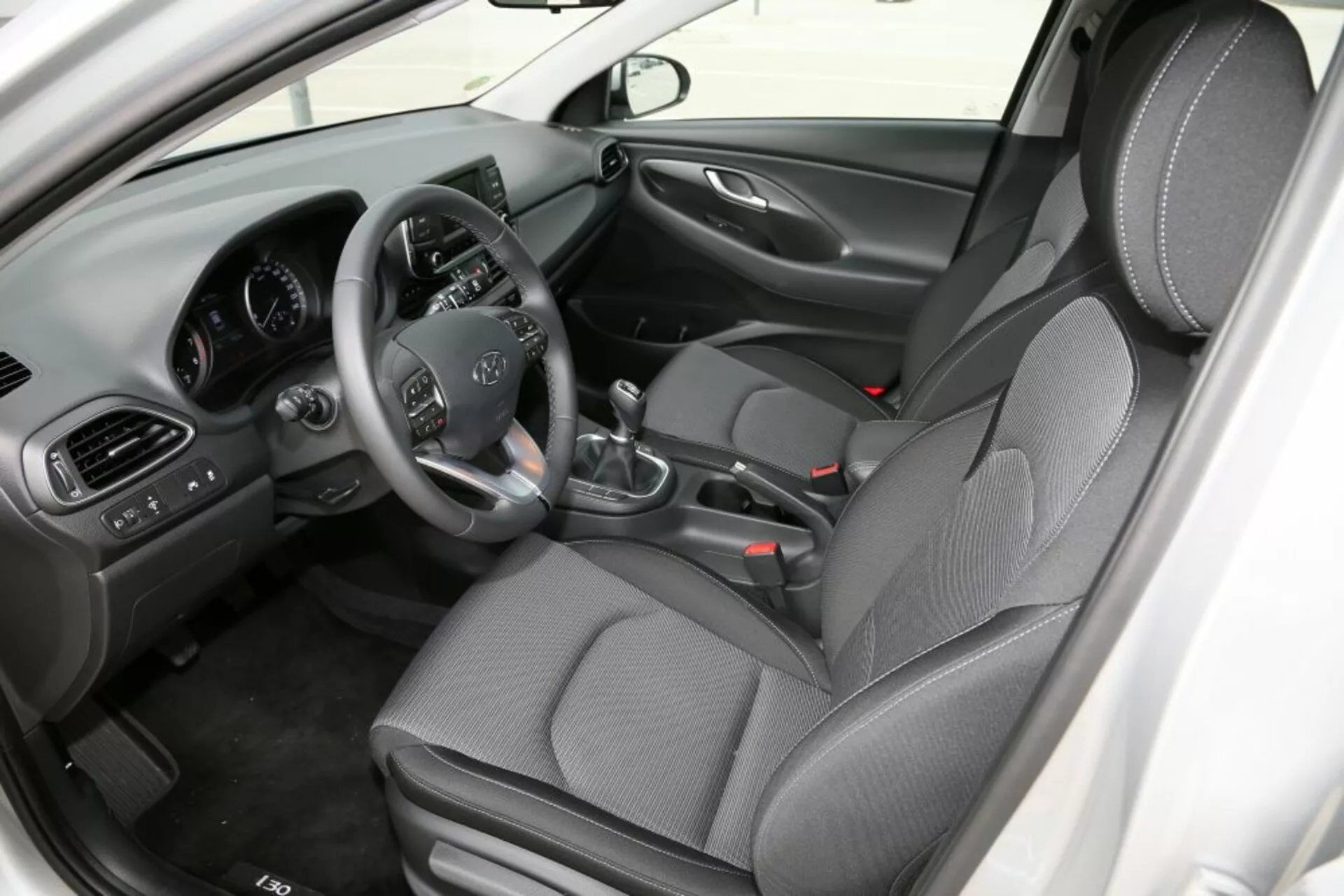 Vista interior de Hyundai i30 2017 (i30-N) centrada en la cabina frontal, mostrando el asiento del conductor con controles en el volante, cambio manual, consola central y asientos de tela estampada