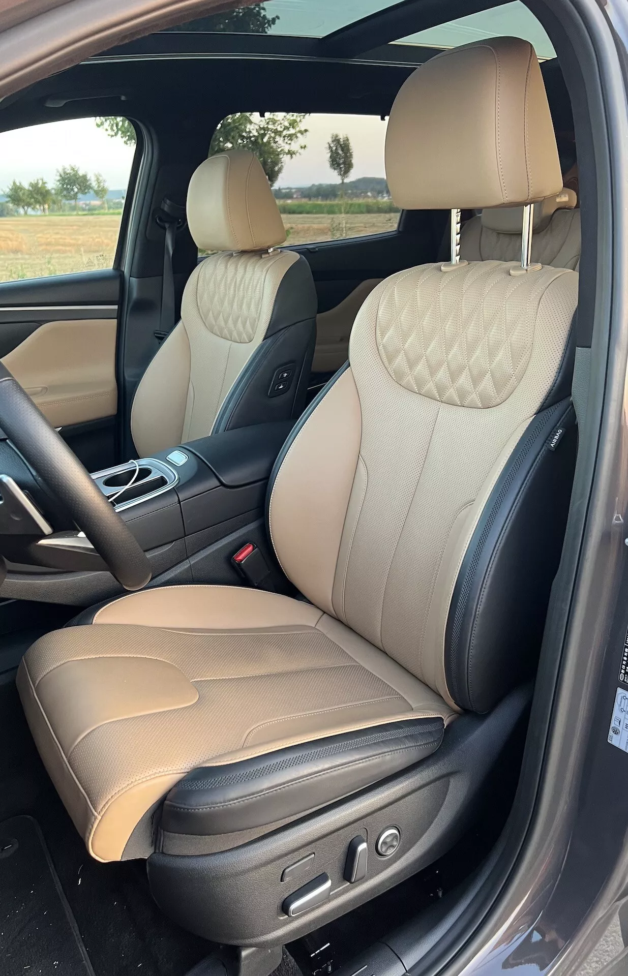 Vista interior de un Hyundai Santa Fe 2020, resaltando el lujoso área del pasajero delantero con asientos de cuero de dos tonos con costuras acolchadas en forma de diamante, controles ajustables eléctricamente y materiales sofisticados como acabados metálicos cepillados y manijas de puertas cromadas.