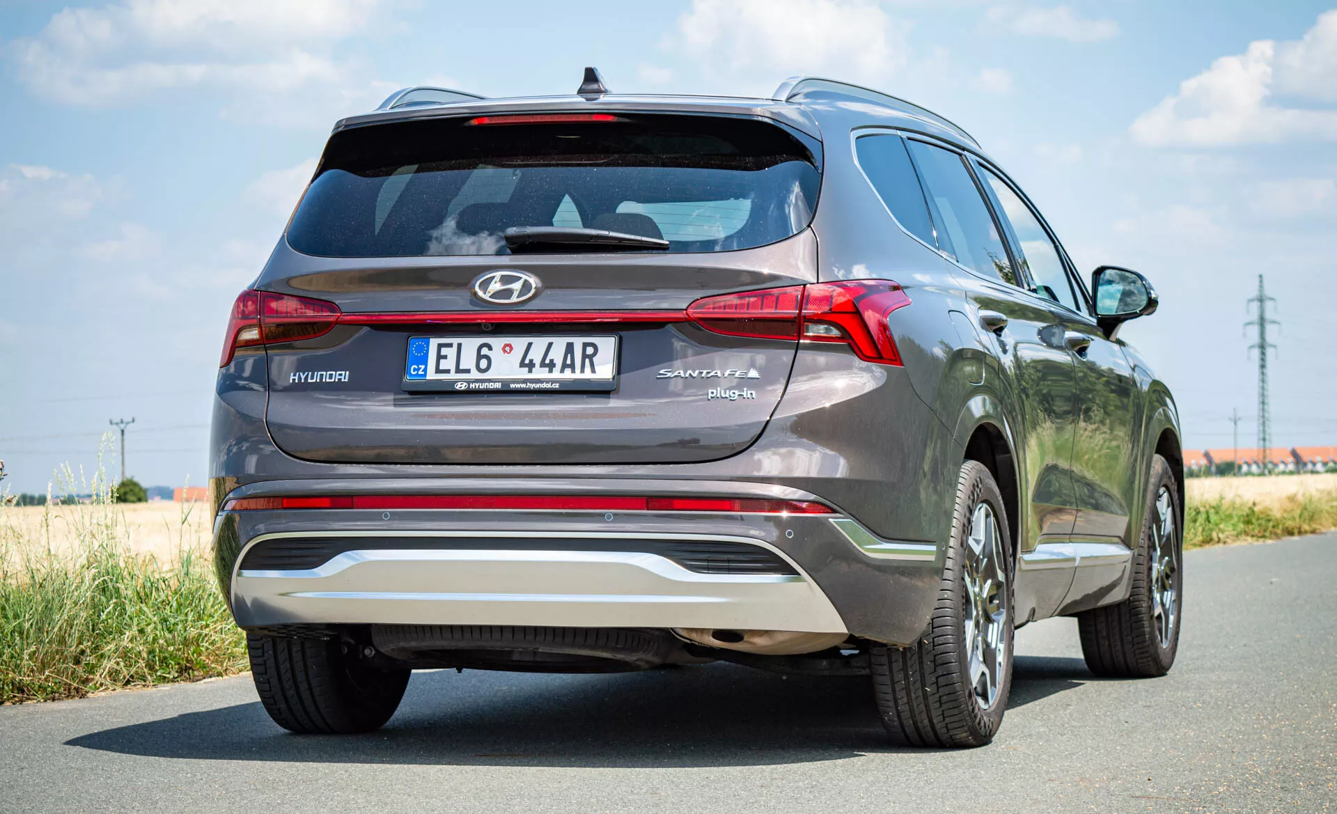 Vista trasera del SUV híbrido Hyundai Santa Fe 2020 con emblema Hyundai en el portón trasero, marca SANTA FE, luces traseras LED distintivas, alerón trasero, placa antideslizante plateada, matrícula central, llantas de aleación y acabado de pintura metálica, capturado en un día despejado con una carretera asfaltada y áreas de césped.