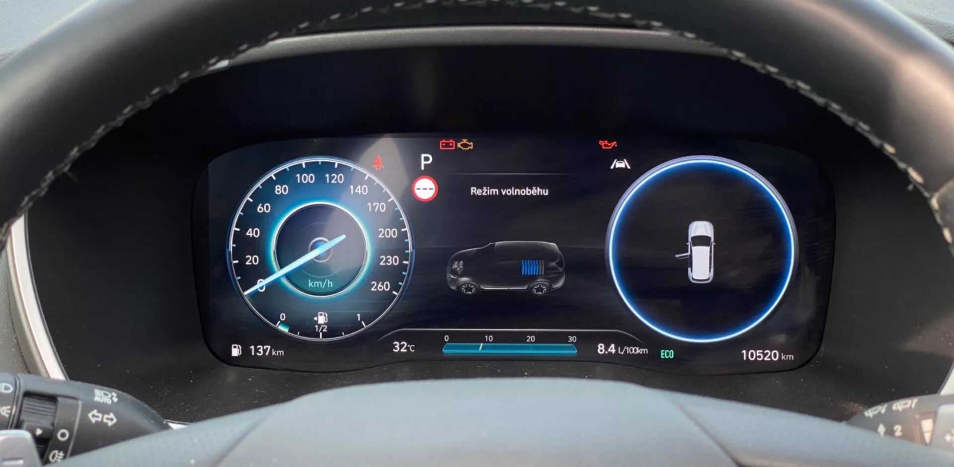 Vista de cerca del moderno panel de instrumentos digital en un Hyundai Santa Fe 2020, tomada desde la perspectiva del conductor. Centrada en la zona del salpicadero, la imagen presenta dos pantallas digitales principales en azul y negro. La pantalla izquierda es un velocímetro que muestra 137 km/h con indicadores adicionales de RPM. La pantalla derecha monitorea el estado del vehículo, incluyendo una alerta de mantenimiento y una advertencia 'Mantener visibilidad'. La sección inferior muestra la temperatura exterior (3,2°C) y el odómetro (10.520 km), junto con un metric de eficiencia de 8,4 litros por 100 kilómetros.