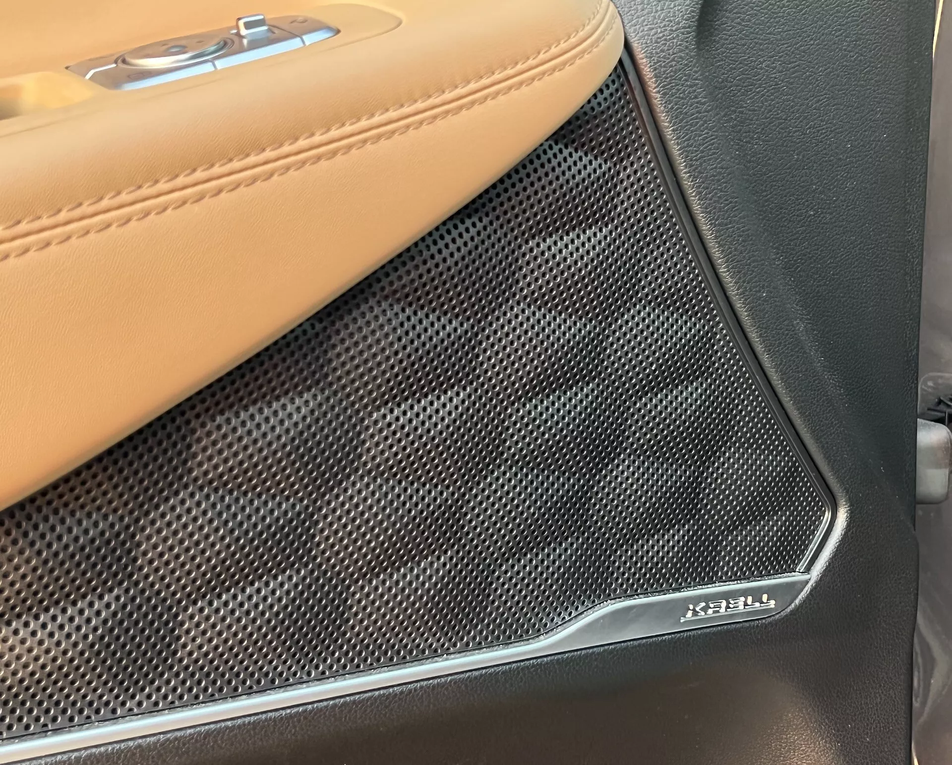 Vista de cerca del panel de la puerta interior del Hyundai Santa Fe 2020, enfocándose en la transición entre la tapicería de cuero beige con costuras en contraste y la rejilla del altavoz Bowers & Wilkins. La cubierta texturizada y perforada del altavoz con el emblema cromado de Bowers & Wilkins destaca el sistema de audio premium y los materiales de lujo del vehículo.