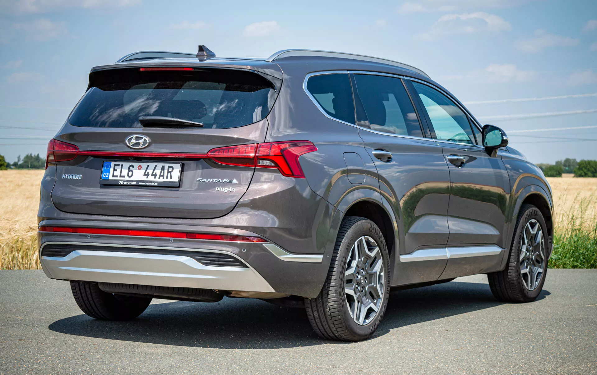 Vista de tres cuartos trasera de un SUV Hyundai Santa Fe 2020 gris, destacando el lado trasero izquierdo. La imagen muestra luces traseras LED prominentes, limpiaparabrisas trasero, desempañador y limpiador, con el emblema de Hyundai y el nombre del modelo 'Santa Fe' cerca de la placa de matrícula, ubicada en el centro. Un adorno plateado añade estilo y un sistema de cámara o sensor de estacionamiento aparece encima de la placa. También son visibles las ruedas de aleación multirradio y los neumáticos en buen estado, indicando un vehículo moderno y bien mantenido. Ideal para listados automotrices, reseñas o contenido enfocado en tecnología.