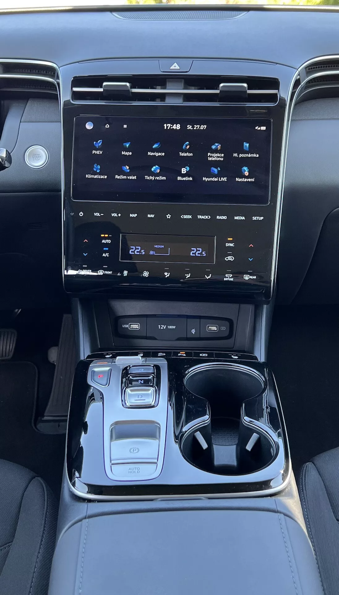 Interior del Hyundai Tucson 2020 mostrando la consola central con un gran sistema de infoentretenimiento táctil, botones de control climático, selector de marchas electrónico, selector de modo de conducción, portavasos, compartimento de almacenamiento e iluminación ambiental.