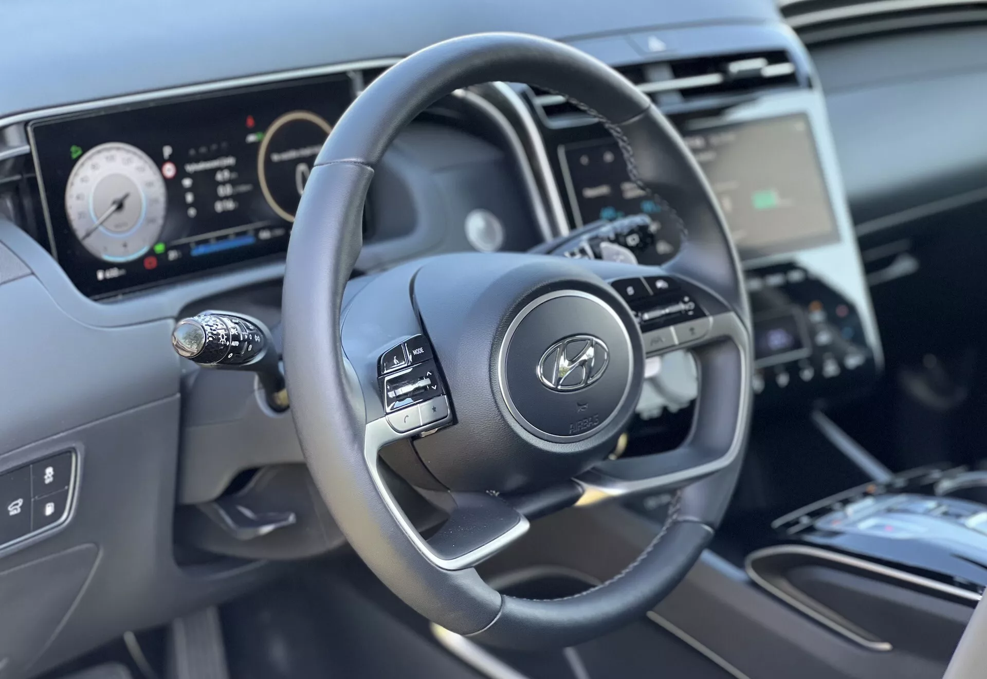 Vista interior del Hyundai Tucson 2020 enfocando en el volante y las características del tablero desde la perspectiva del conductor, resaltando el diseño de tres radios con botones de control, el cuadro de instrumentos digital, y vista parcial de la consola central y control del clima.