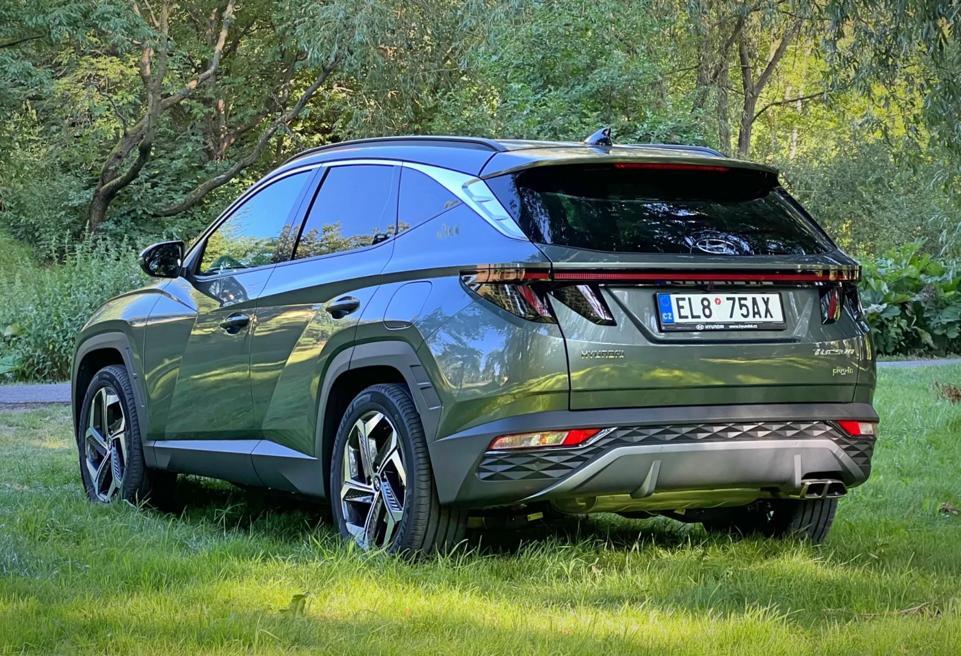 Vista trasera tres cuartos del Hyundai Tucson 2020 destacando las luces traseras LED, sensores de estacionamiento, doble escape, alerón trasero deportivo y barras de techo, estacionado al aire libre sobre césped mostrando el diseño aerodinámico y características avanzadas de un moderno SUV crossover para aventuras al aire libre y uso práctico.