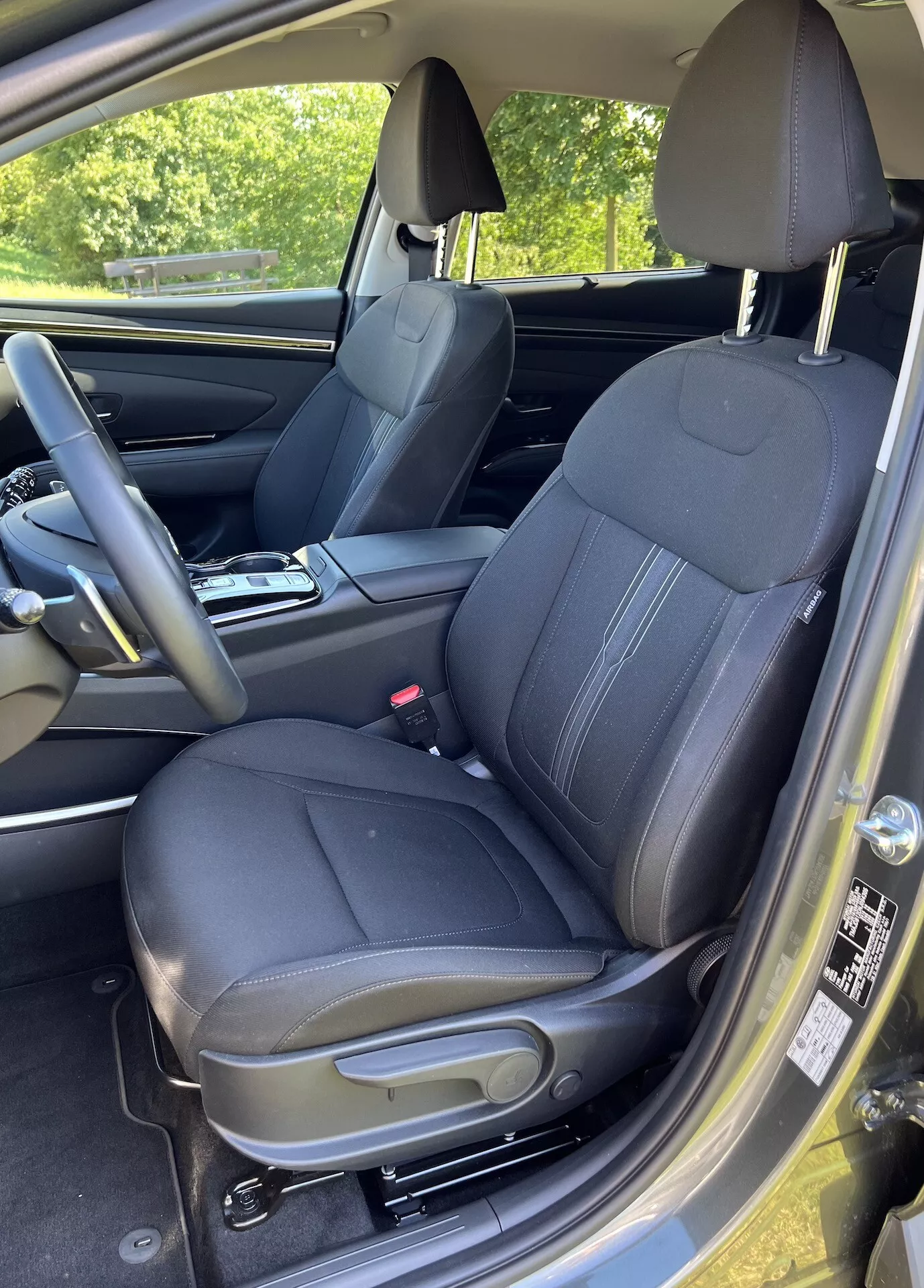 Vista interior del Hyundai Tucson 2020 enfocando el asiento del conductor con tapicería de cuero acolchado, reposacabezas integrado y controles en el panel de la puerta para ventanas y espejos eléctricos, capturado desde una perspectiva ligeramente elevada y angular mostrando controles de ajuste del asiento, parte del volante, suelo alfombrado y un atisbo de iluminación exterior
