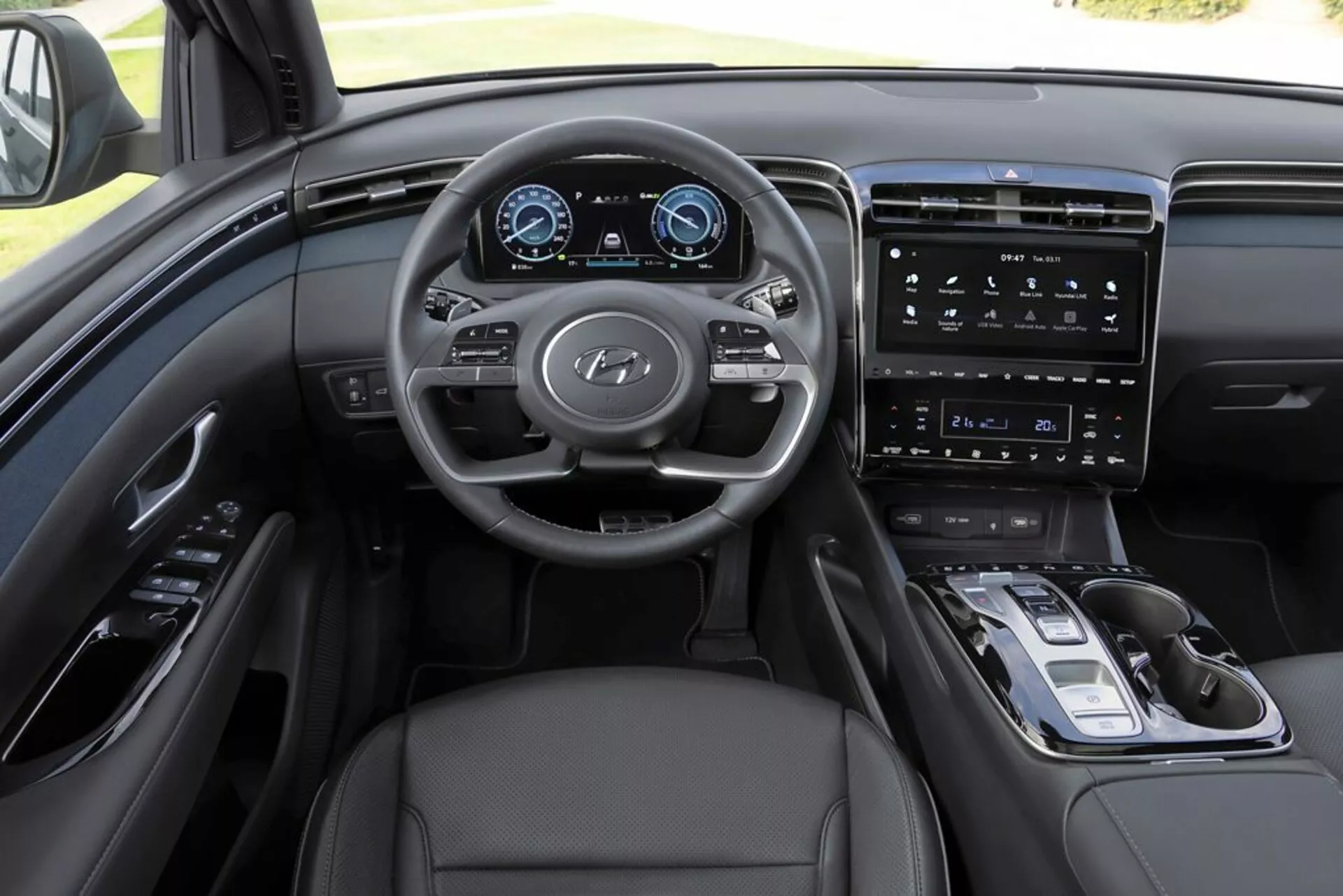 Vista interior del Hyundai Tucson 2020 desde la perspectiva del conductor, destacando el tablero de mandos, volante multifuncional con logo de Hyundai, cuadro de instrumentos digital, sistema de infoentretenimiento con pantalla táctil vertical, controles minimalistas en la consola central, selector de marchas electrónico, tapicería de cuero y sofisticado esquema de color monocromático