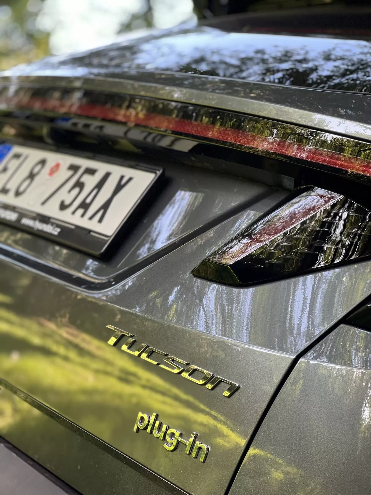 Vista detallada de la sección trasera de un Hyundai Tucson 2020 híbrido enchufable, mostrando la tapa del maletero, el conjunto de iluminación trasera con luces LED, acabado brillante oscuro y detalles que indican condiciones de estacionamiento al aire libre