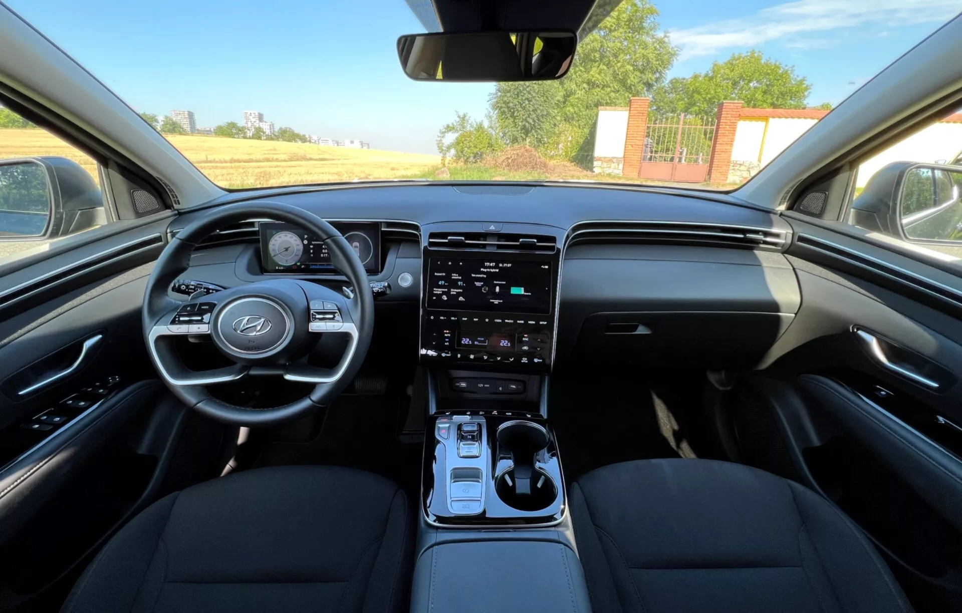 Interior del Hyundai Tucson 2020 mostrando asientos delanteros, volante con logo del fabricante y botones de control, cuadro de instrumentos digital, sistema de infotenimiento táctil vertical en consola central, palanca de cambios automática y diseño de tablero en dos tonos desde una perspectiva a nivel de los ojos similar a la del conductor o pasajero delantero