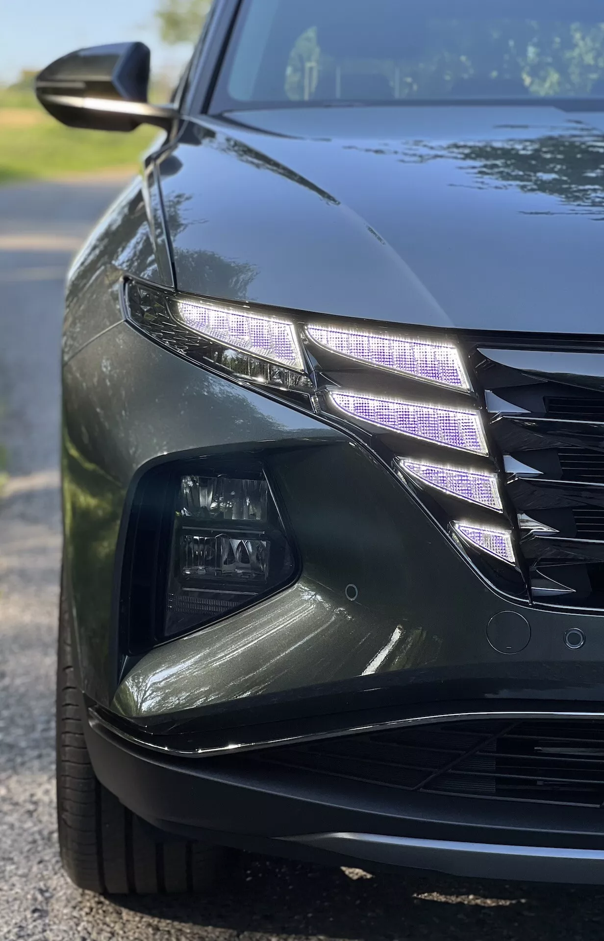 Vista en ángulo cercano de un Hyundai Tucson 2020 mostrando un intrincado diseño de faros LED y parte de la parrilla con un acabado brillante bajo condiciones de poca luz, ilustrando características de autos de lujo y tecnología moderna de iluminación automotriz.