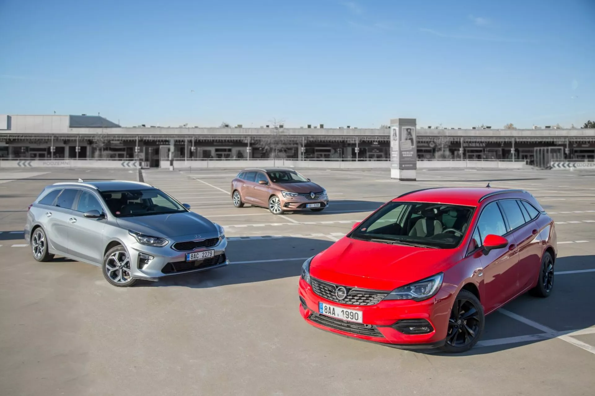Tres modelos de Kia Ceed de 2009 incluyendo un hatchback rojo, un crossover dorado y una camioneta familiar plateada estacionados en un lote en la azotea, fotografiados desde una posición elevada mostrando el diseño frontal, los perfiles laterales y la longitud del vehículo