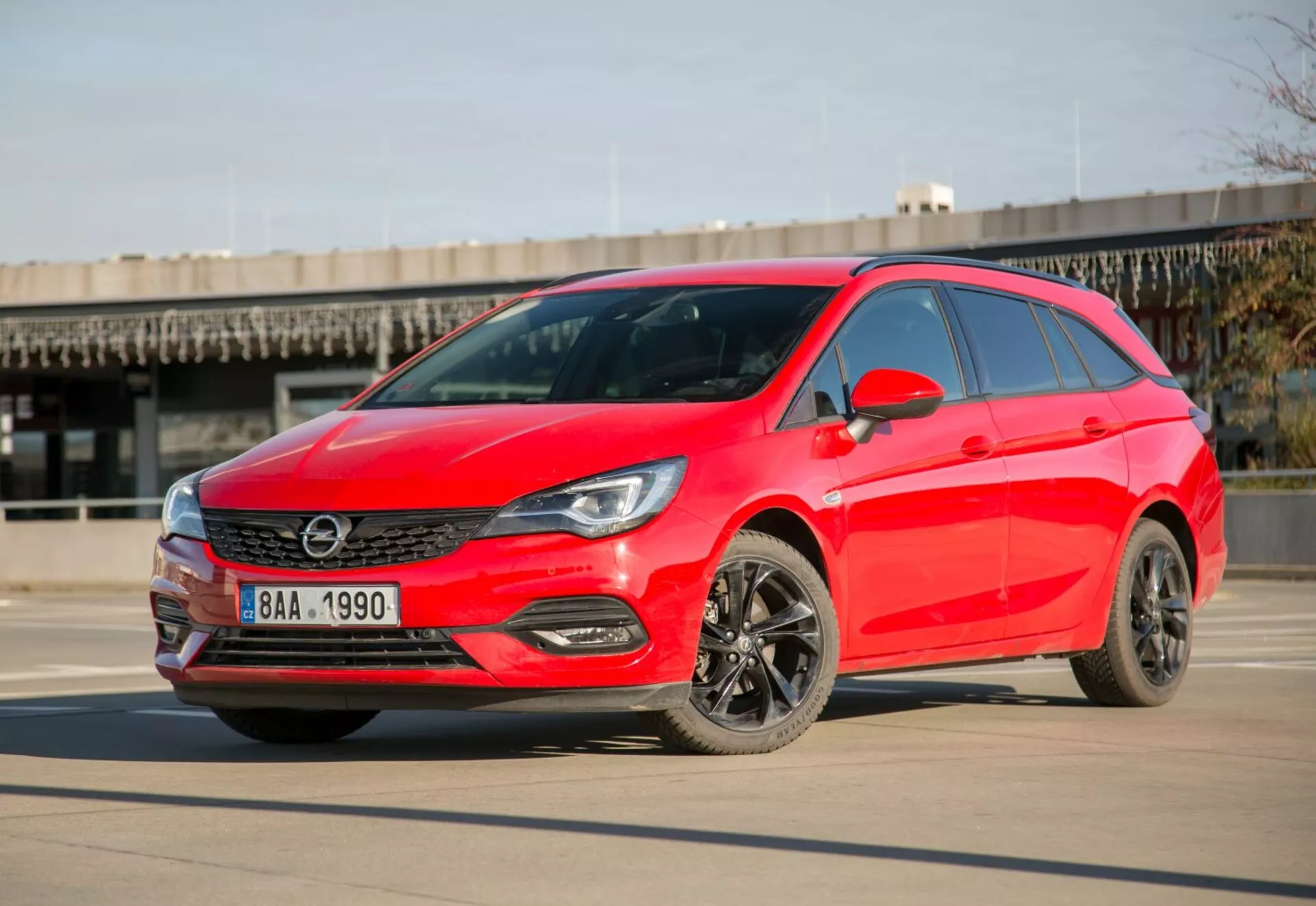 Hatchback rojo brillante Kia Ceed de 2009 aparcado en hormigón liso bajo cielos despejados, mostrando faros LED, parrilla elegante, ruedas de aleación oscuras y diseño aerodinámico moderno desde un ángulo frontal de tres cuartos durante el día.