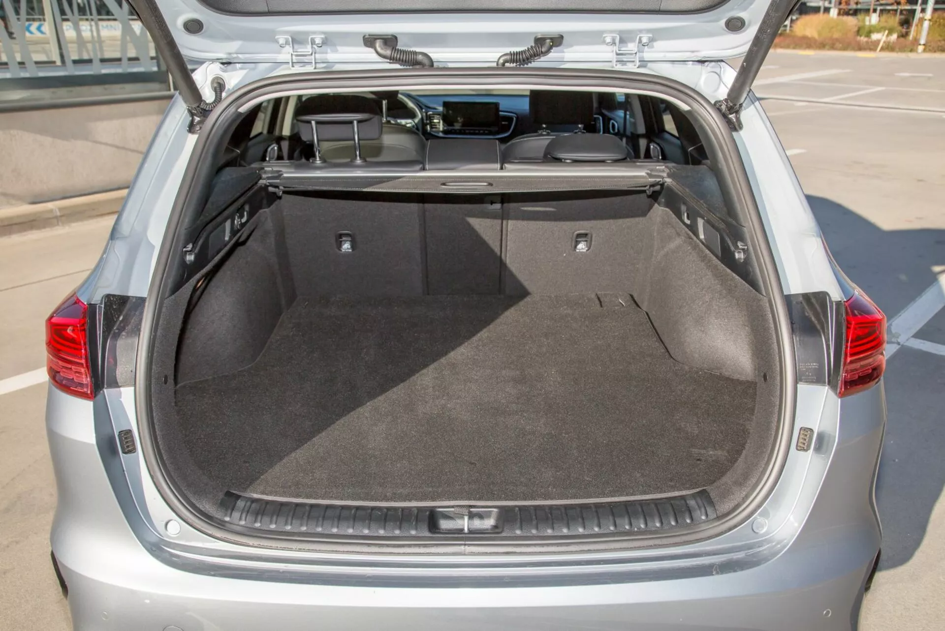 Compartimento trasero del maletero de un hatchback Kia Cee'd 2009 con la tapa abierta, mostrando un espacio de carga amplio y limpio, alfombrado, cobertor retráctil y posible iluminación interior