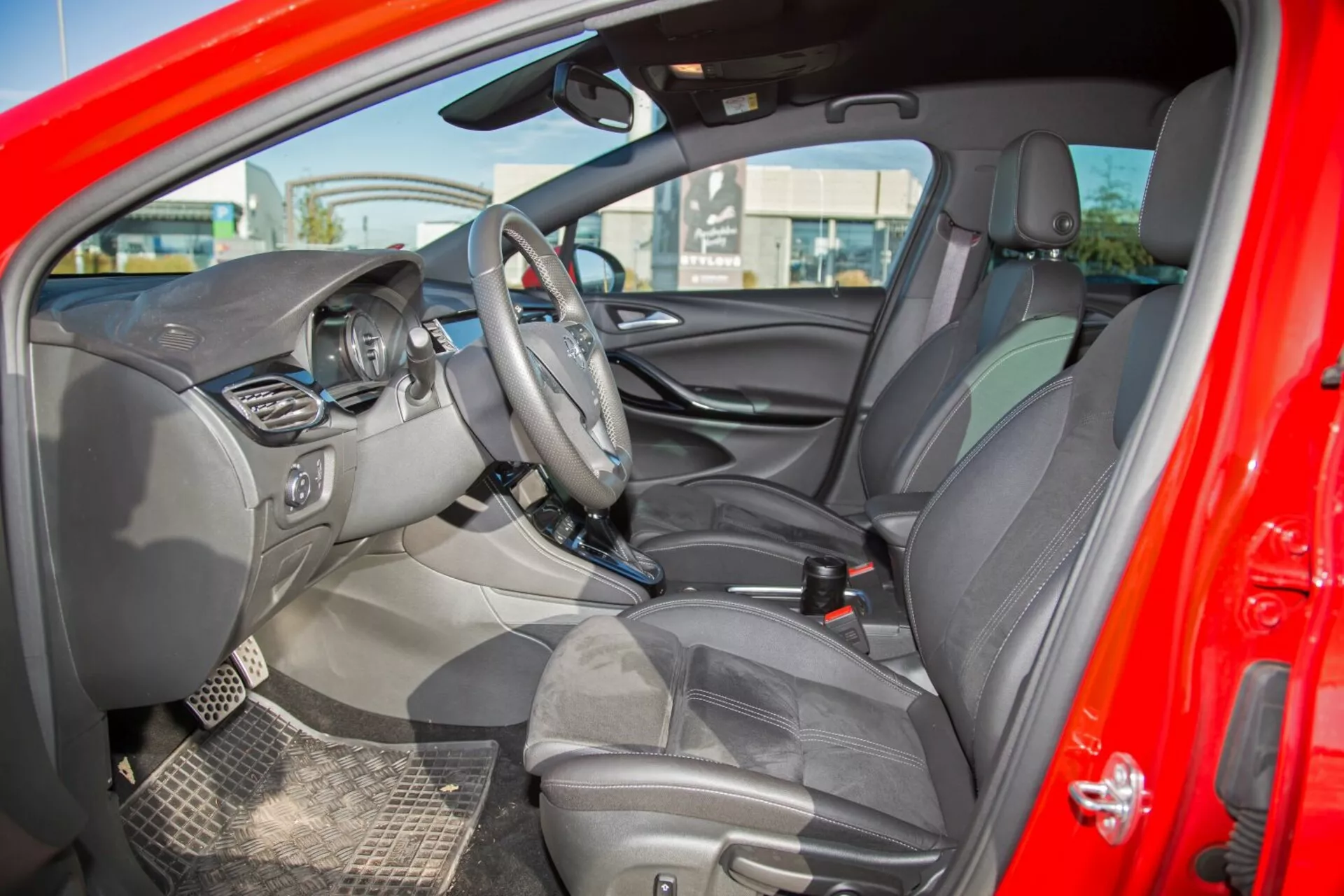 Interior del Kia cee'd 2009 mostrando volante con controles, pantalla de infoentretenimiento central, cluster de instrumentos visible, consola central con controles adicionales, asientos tapizados con reposacabezas, interior detallado de la puerta con controles, esquema de colores en dos tonos, vista del espejo retrovisor y del espejo lateral del conductor, alfombrillas duraderas e indicadores de airbag, capturando un diseño integral y características enfocadas en tecnología desde una perspectiva lateral exterior
