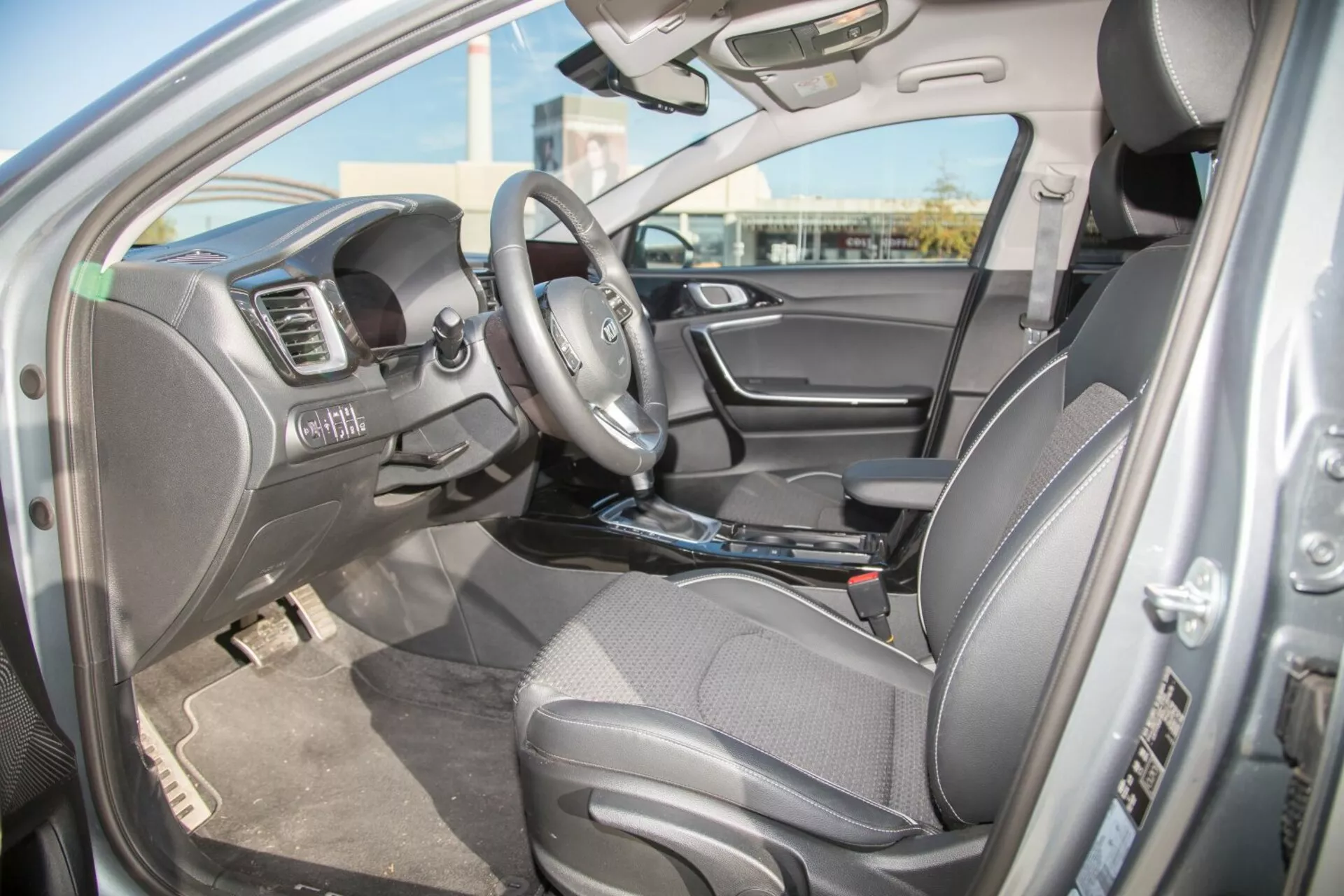 Vista interior del Kia Cee'd 2009 desde el lado del conductor mostrando el asiento, volante con controles integrados y características del salpicadero incluido el sistema multimedia