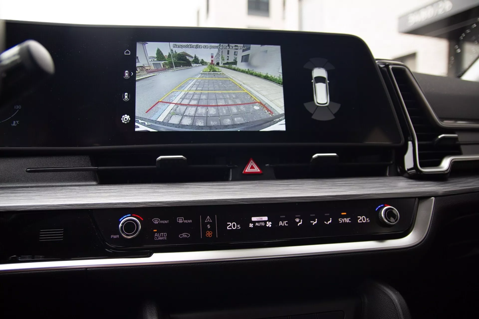 Vista interior del Kia Sportage 2022 desde el asiento del conductor destacando la pantalla táctil del sistema de infotenimiento con salida de cámara trasera, panel de control del clima y diseño estéticamente atractivo con detalles cromados y acabados brillantes