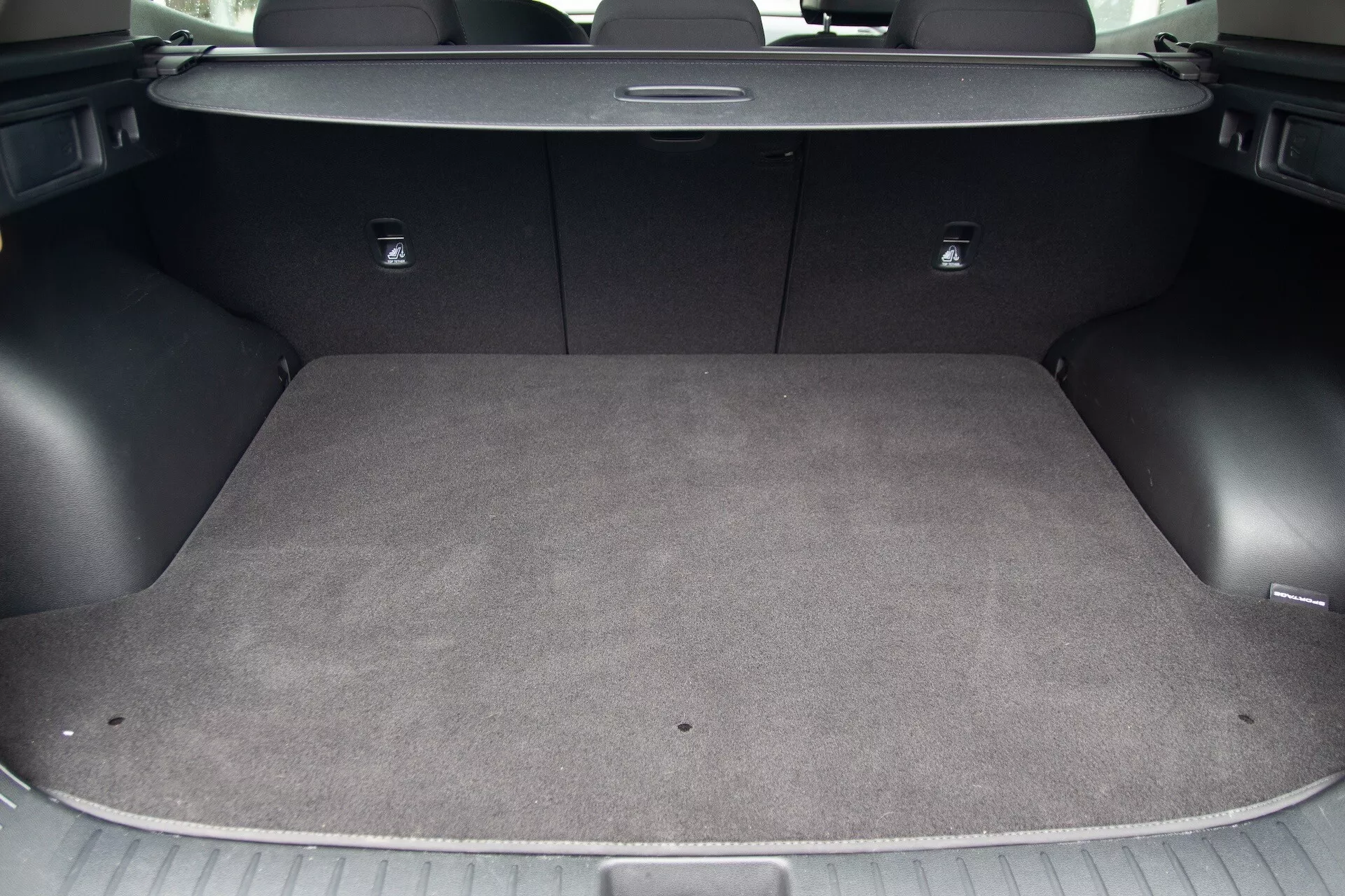 Vista del área de carga del Kia Sportage 2022 que muestra el interior alfombrado, superficie de carga plana, ganchos integrados para amarrar, puntos de anclaje para asientos infantiles con sistema LATCH y asientos traseros abatibles 60/40 para espacio de carga flexible