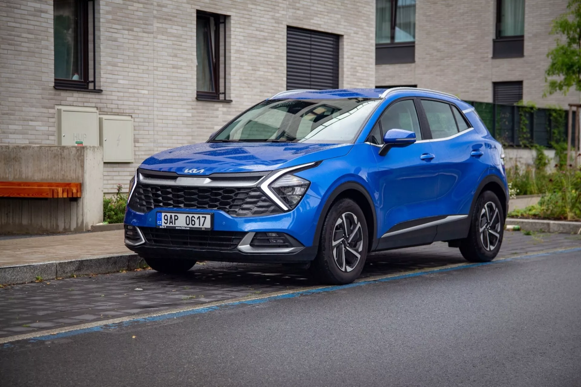 SUV crossover compacto Kia Sportage 2022 en azul, estacionado en una calle mojada mostrando su vista frontal tres cuartos dinámica con luces diurnas LED, capó esculpido y ruedas de aleación.