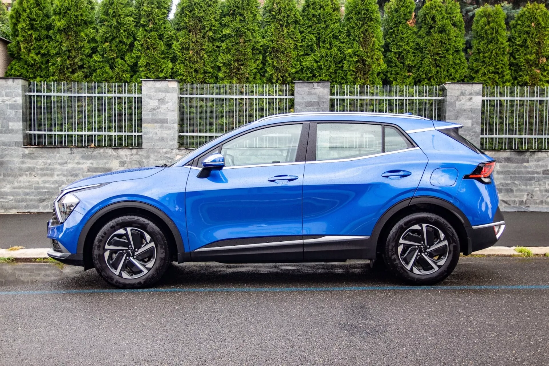SUV crossover Kia Sportage 2022 en azul brillante, mostrando su diseño elegante y compacto con una línea de techo inclinada al estilo de un coupé, capó contorneado, unidades de faros LED, ruedas de aleación de cinco radios y mejoras aerodinámicas como un spoiler trasero, en un entorno suburbano.