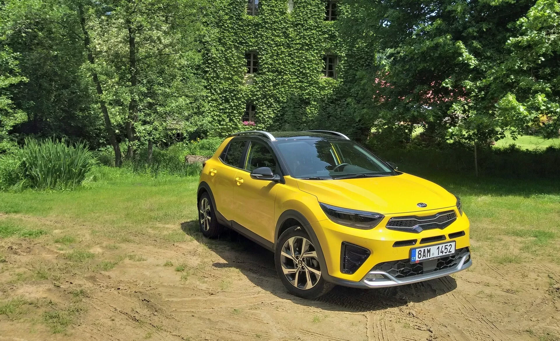 SUV crossover amarillo vibrante Kia Stonic 2017 en vista frontal de tres cuartos destacando su parrilla frontal, faros LED, capó y lado del conductor, ubicado contra un fondo natural con luz solar en suelo despejado, mostrando capacidades todoterreno, ruedas de aleación deportivas y elementos de diseño moderno.