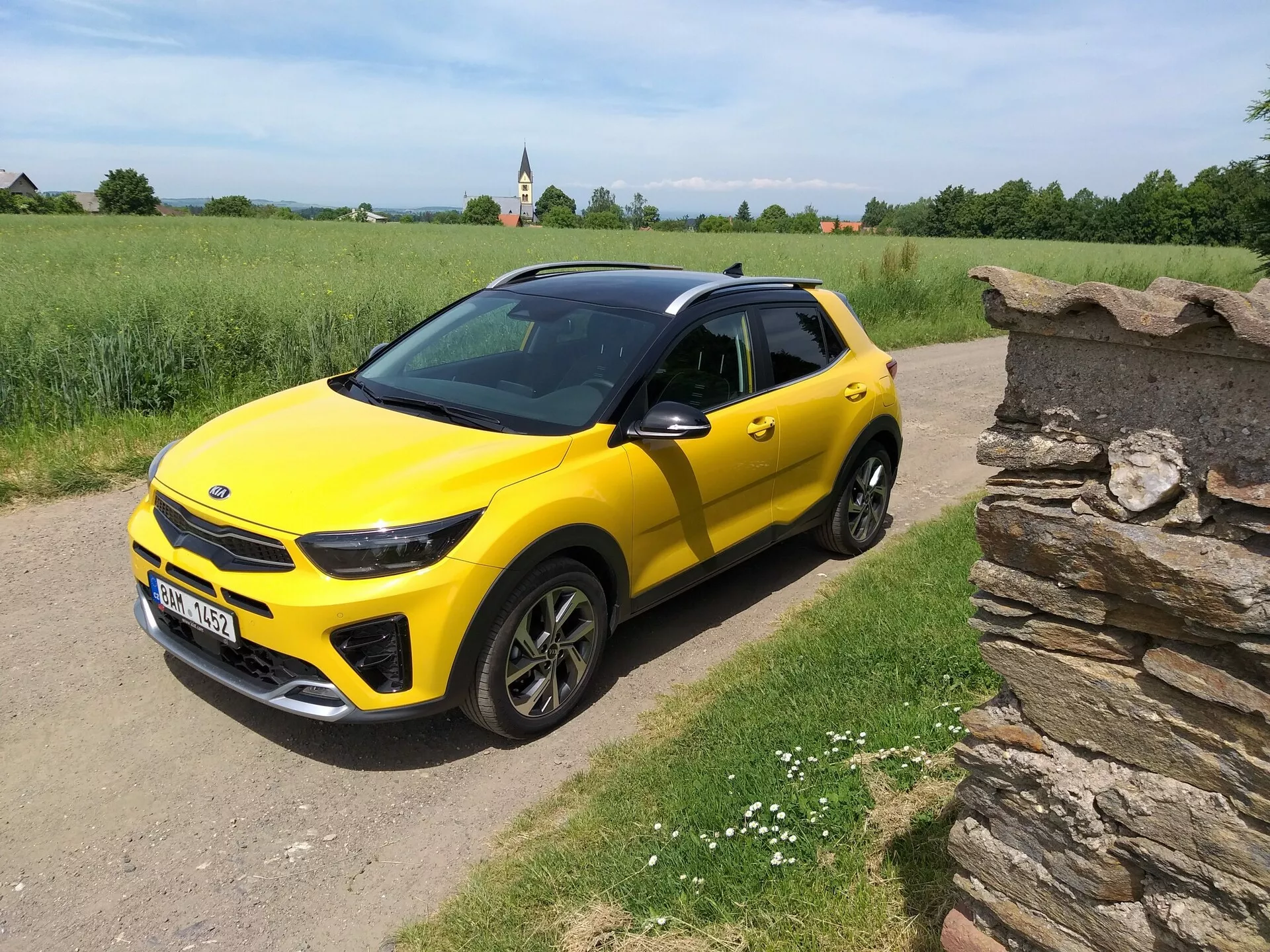 SUV compacto Kia Stonic 2017 de color amarillo brillante con techo negro, mostrando su elegante diseño y contornos dinámicos desde un ángulo frontal de tres cuartos en un camino rural