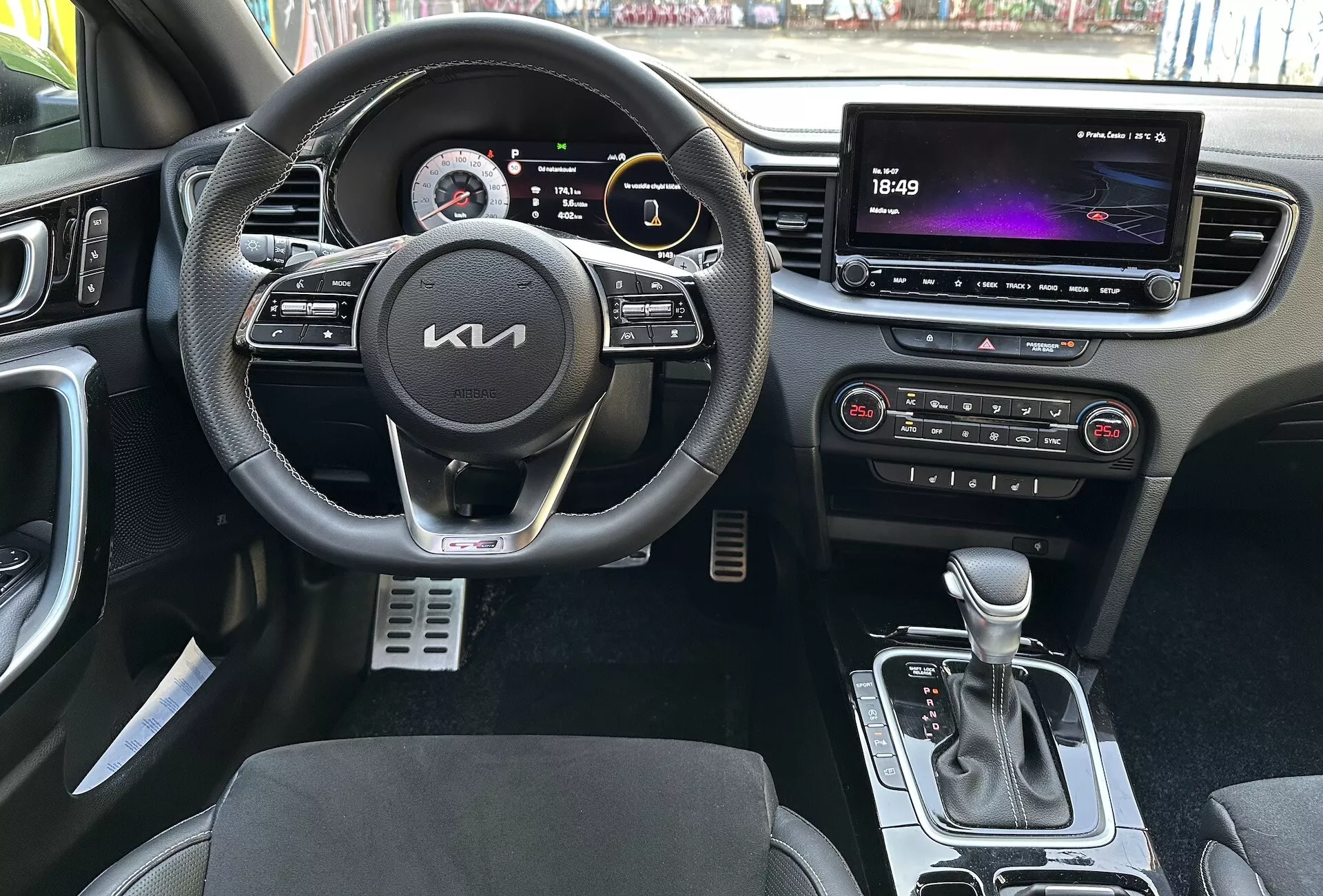 Vista interior del Kia XCeed 2022 destacando características centradas en el conductor como un volante multifuncional forrado en cuero con botones para multimedia y control de crucero, un cuadro de instrumentos digital, un sistema de infotenimiento táctil grande, controles automáticos de clima, palanca de cambios automática, asientos con tapicería bicolor y pedales deportivos de metal desde una perspectiva en primera persona.