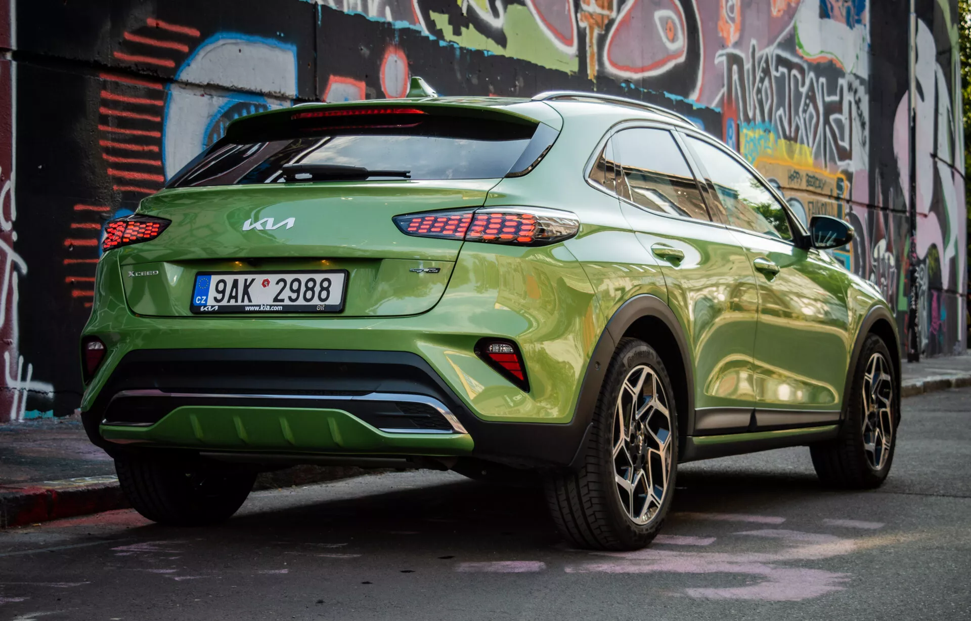 SUV crossover moderno Kia XCeed 2022 aparcado en diagonal mostrando su cuarto trasero derecho, con pintura verde vibrante y ruedas de aleación oscuras, que demuestra el perfil lateral del vehículo, el diseño trasero, luces traseras LED, ventanas tintadas, un alerón de techo y un posible difusor trasero