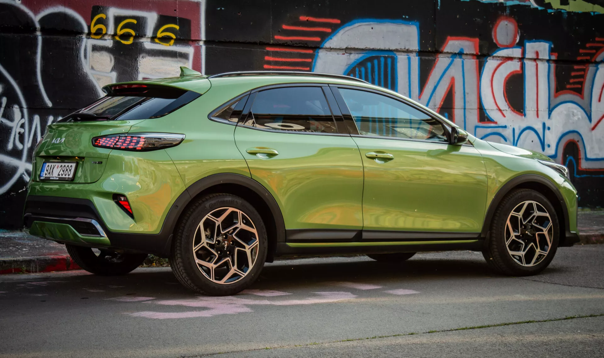 Vista lateral del Kia XCeed 2022 destacando el diseño de la rueda trasera, pintura metálica verde, luces traseras LED y estilo de SUV compacto con características aerodinámicas contra un fondo de arte callejero urbano.