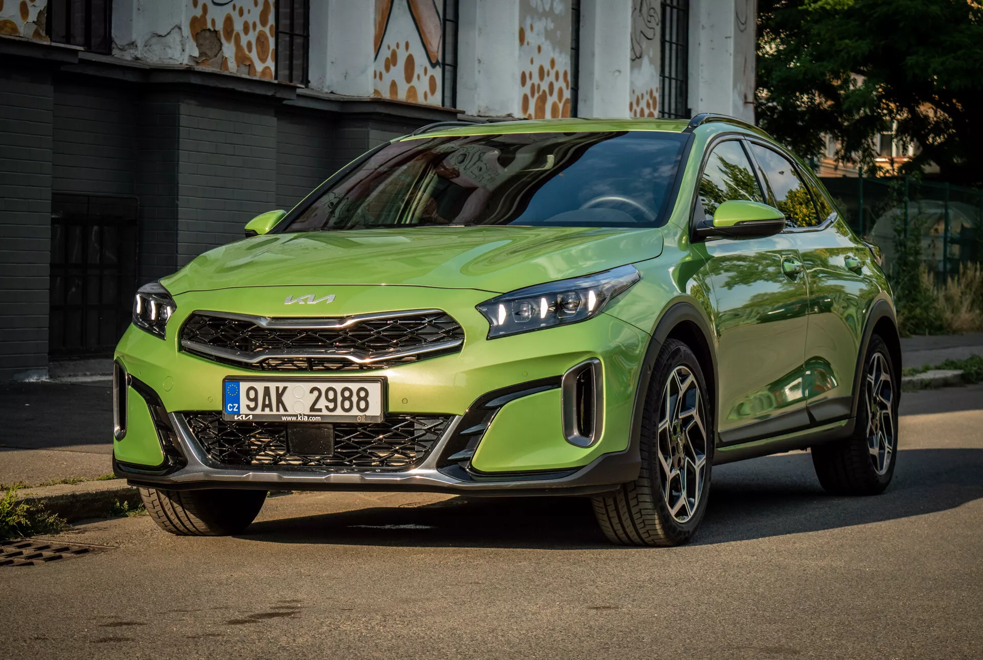 Kia XCeed 2022 en verde lima vibrante con faros LED, parrilla frontal prominente con emblema de la marca, paragolpes delantero deportivo y grandes ruedas de aleación, centrado en una carretera pavimentada con un fondo urbano