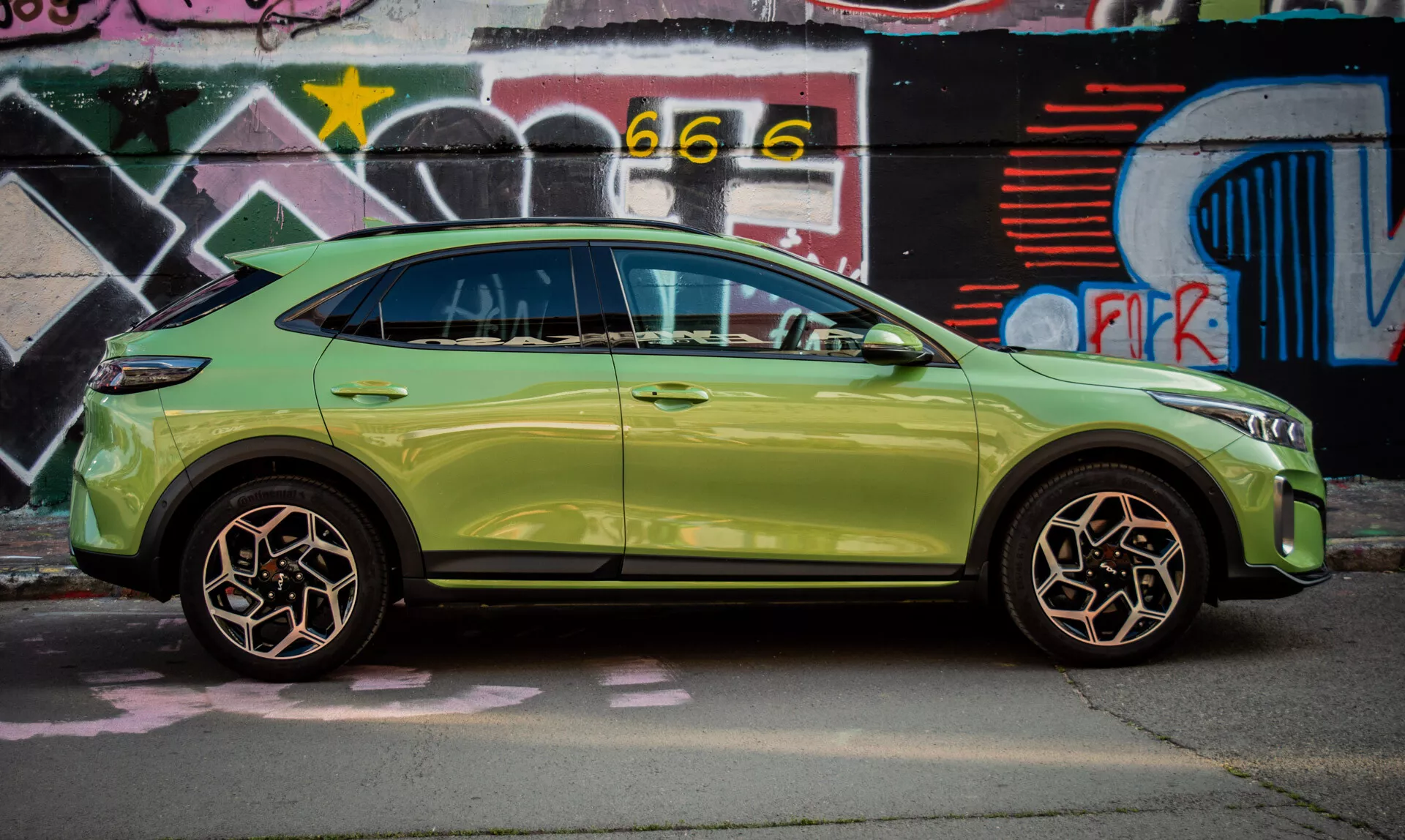 SUV compacto Kia XCeed de 2022 en verde lima aparcado junto a una pared cubierta de grafitis, mostrando su elegante diseño y características avanzadas como entrada sin llave e intermitentes integrados en los espejos laterales.