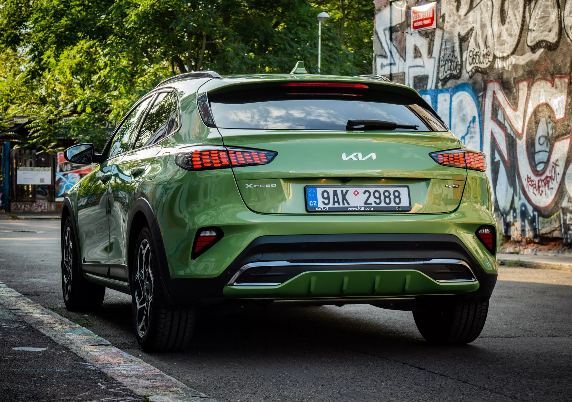 Vista trasera de un crossover/SUV Kia XCeed verde del 2022 mostrando la marca, diseño de luces traseras LED, colocación de placa de matrícula, estética del parachoques inferior y acabado brillante en una calle urbana.