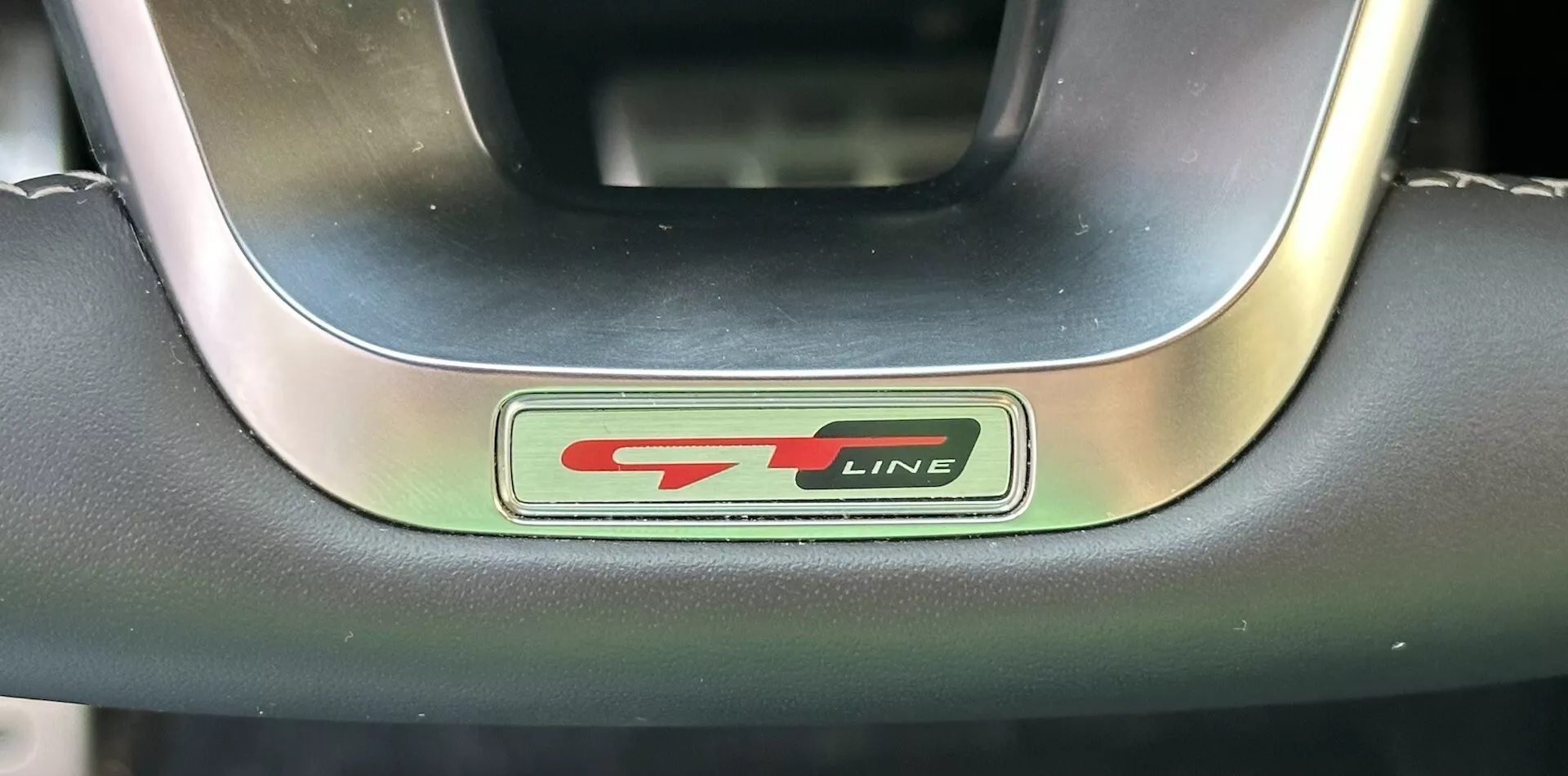 Primer plano del emblema del volante GT-Line Kia XCeed 2022 mostrando letras metálicas y negras con un acento rojo deportivo, rodeado de un volante premium de cuero y metal