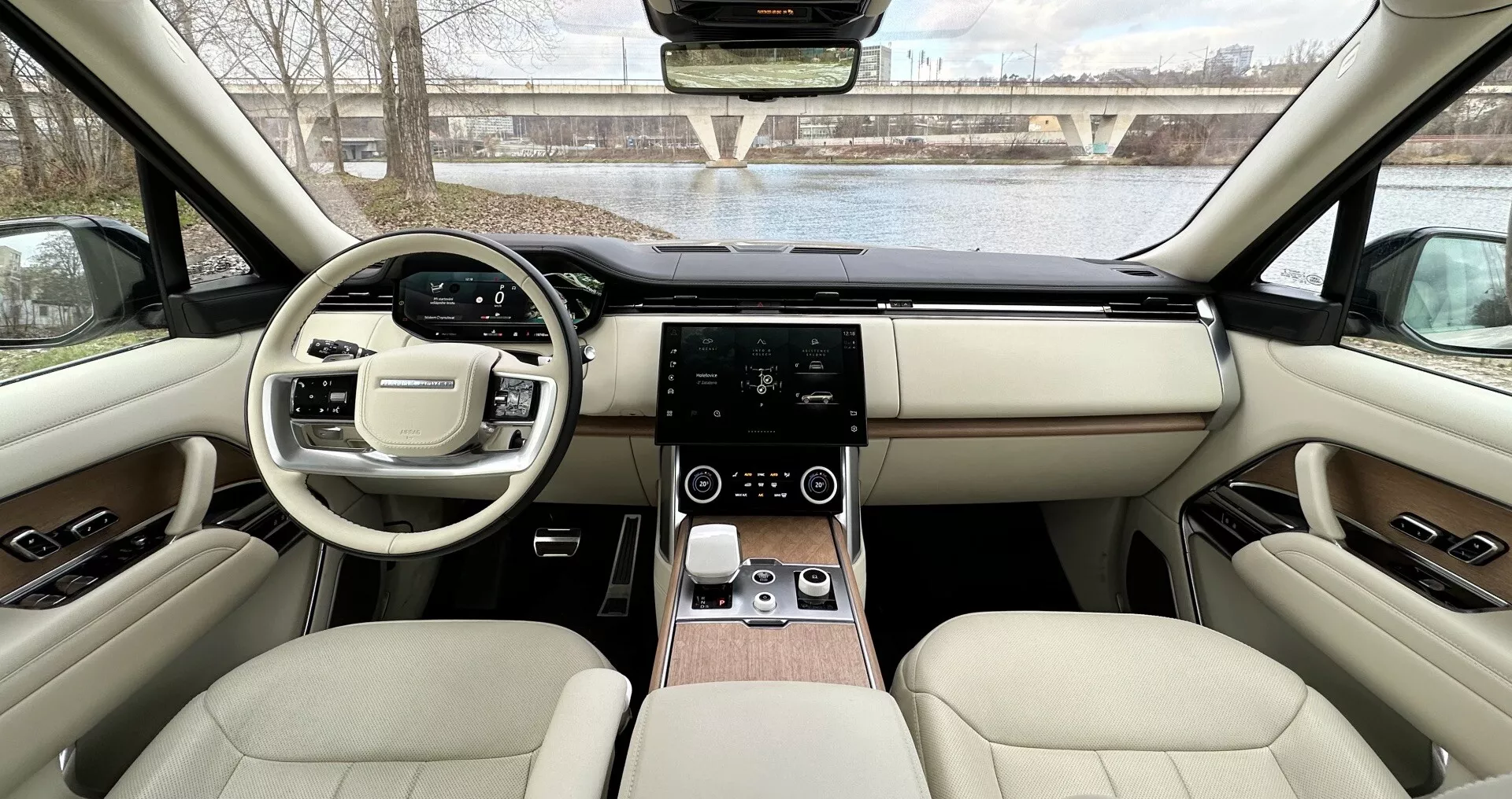 Vista interior del Land Rover Range Rover 2021 desde los asientos traseros hacia el tablero mostrando diseño simétrico, volante con botones multifunción, sistema de infotenimiento táctil, control digital de clima, tapicería de cuero lujoso con acentos de madera, y características tecnológicas avanzadas