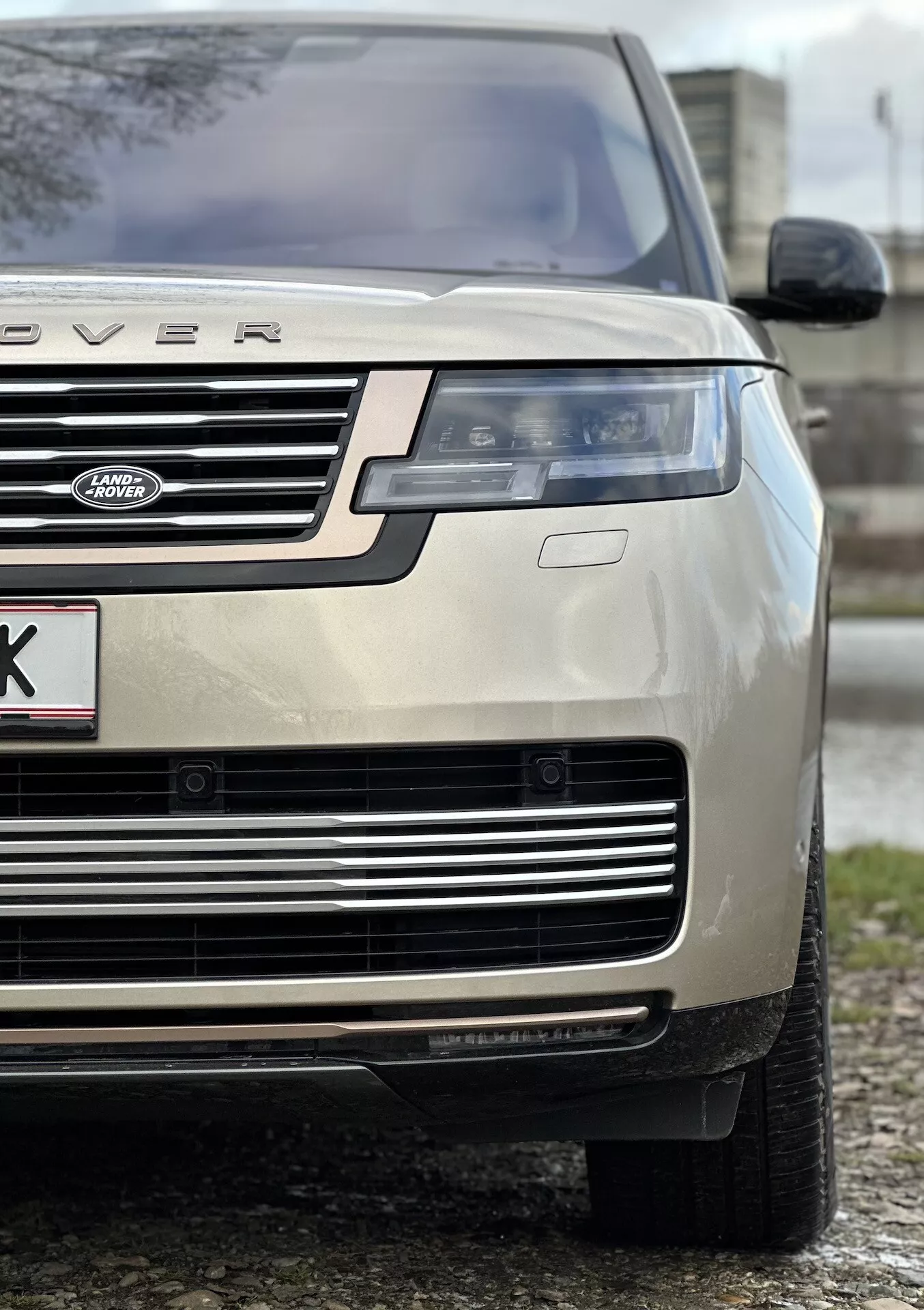 Primer plano de un Land Rover Range Rover color oro del año 2021, destacando el cuarto frontal izquierdo, enfatizando la altura y postura del vehículo con foco en el capó, la parrilla, el faro LED, el paragolpes y el neumático para toda estación, indicativo de lujo y capacidad todoterreno.