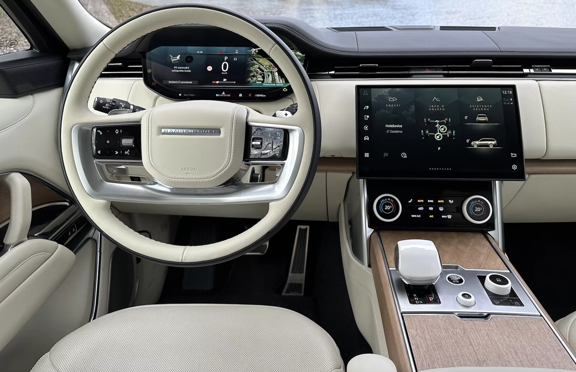Vista interior del Land Rover Range Rover 2021 mostrando el volante moderno con botones multifunción, cuadro de instrumentos digital, pantalla táctil de infotainment central grande, control automático del clima y diseño de cabina de dos tonos de alta gama