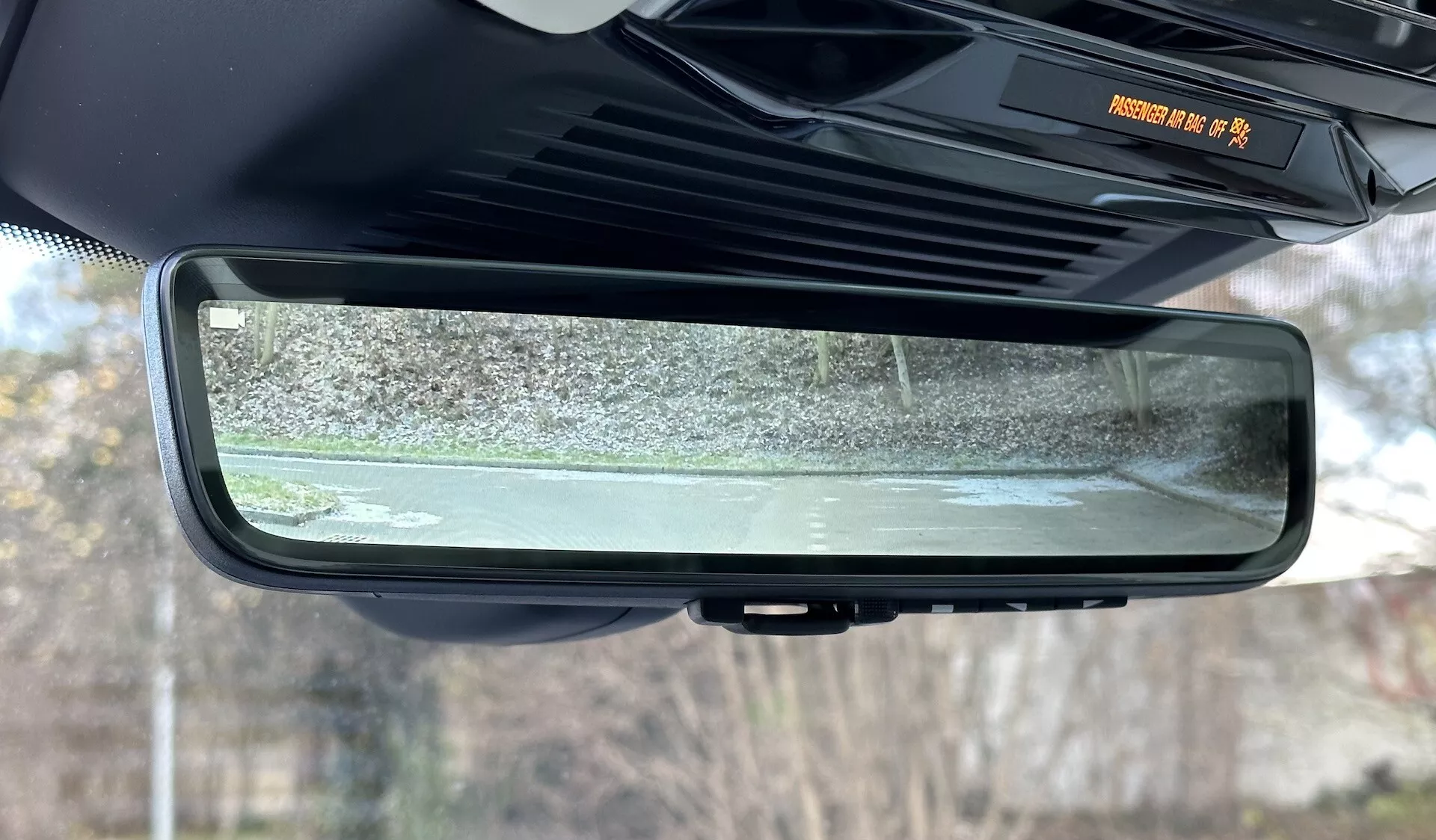 Vista detallada del espejo retrovisor auto-dimable electrocrómico dentro de un Range Rover 2021, destacando su diseño sin marco, características del interior de la cabina y la escena reflejada de los alrededores exteriores estacionarios