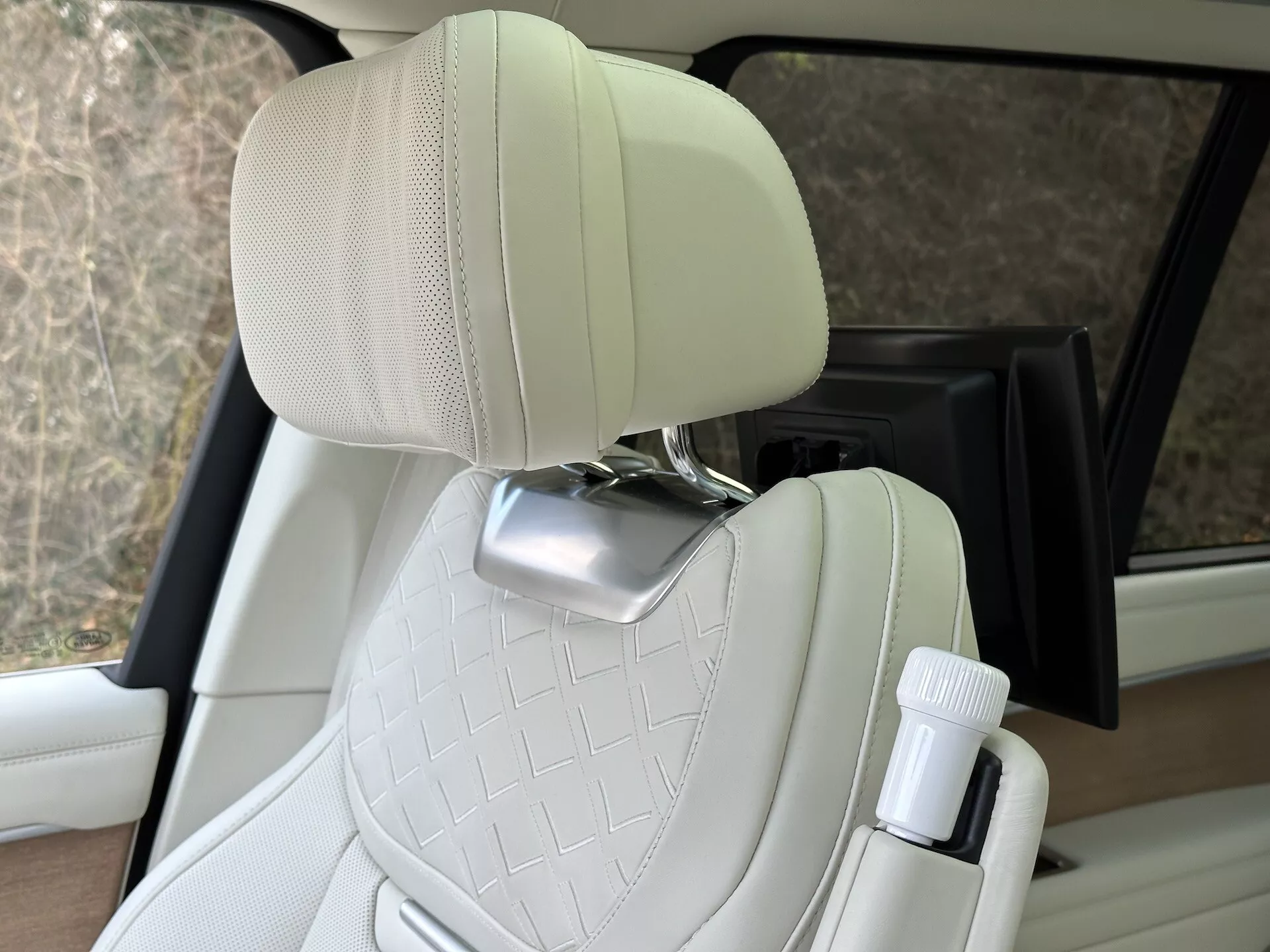 Vista interior del Land Rover Range Rover 2021 destacando el asiento del pasajero de cuero crema acolchado con soporte para la cabeza de cromo y portabotellas en la puerta, mostrando diseño de vehículo de lujo y características de comodidad