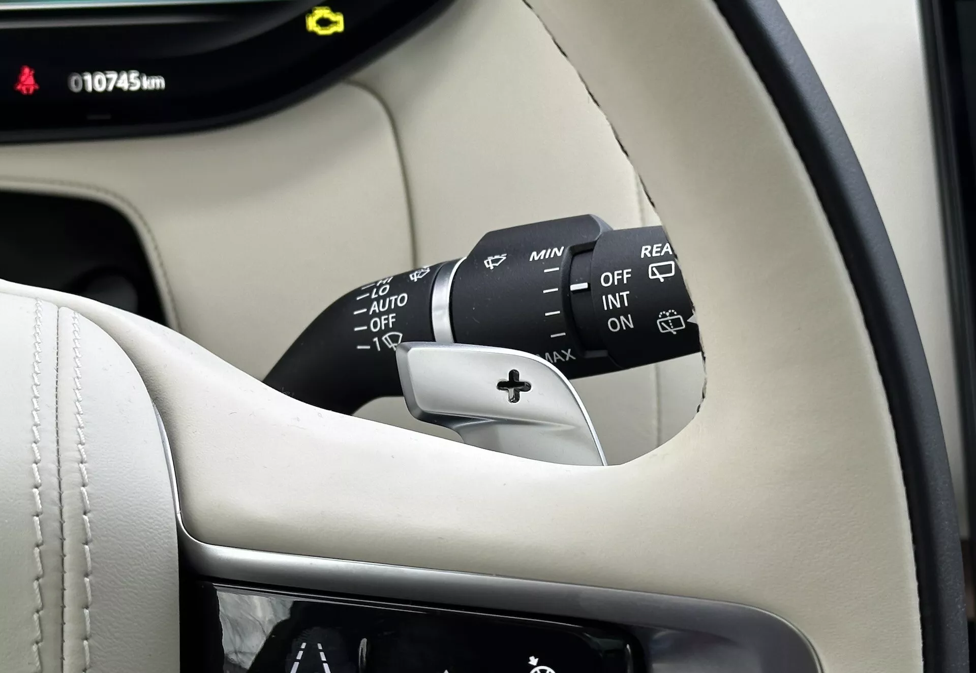 Vista detallada del interior del Land-Rover Range-Rover 2021 mostrando la columna del volante, la palanca de control del limpiaparabrisas con múltiples ajustes incluyendo OFF, INT, ON, ajustadores de velocidad y AUTO para limpiaparabrisas automáticos sensor de lluvia, más una opción de limpiaparabrisas trasero. Parte visible del panel de instrumentos muestra 10745 km, contra un interior premium de color negro y crema.
