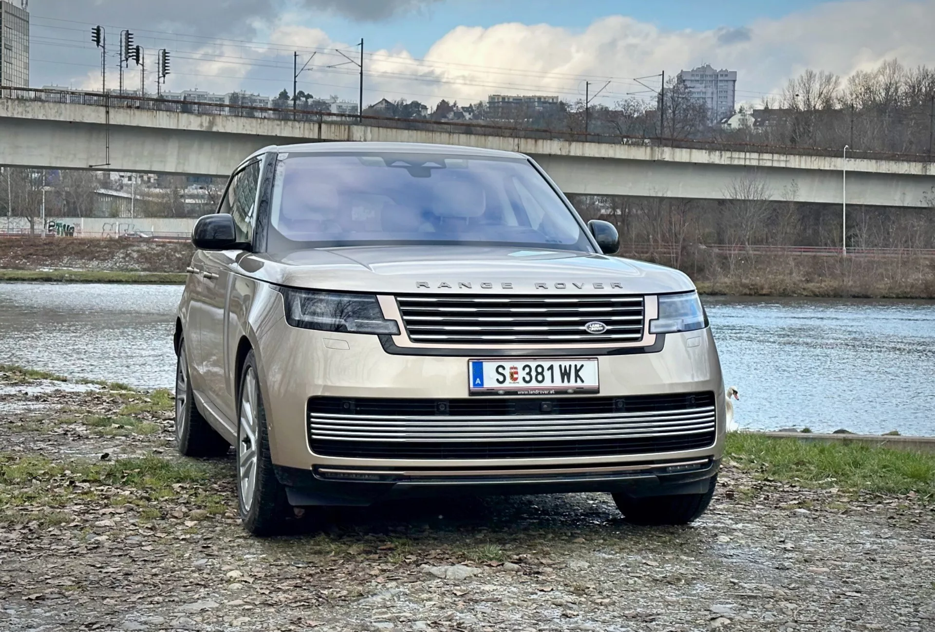 SUV de lujo Range Rover 2021 estacionado al aire libre cerca de un río y puente en un entorno urbano, mostrando su diseño moderno, parrilla frontal y elegantes faros LED