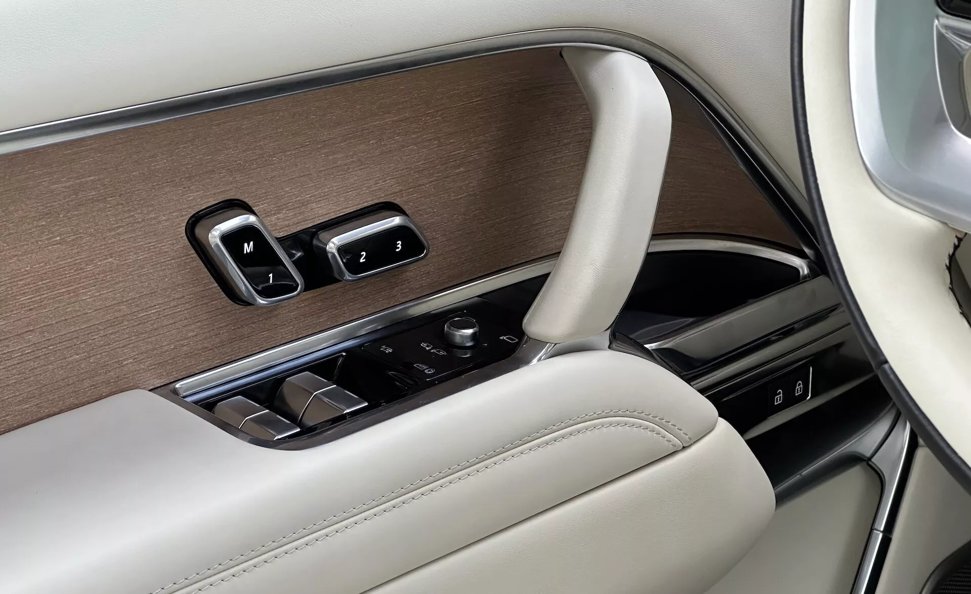 Detalle del interior del Land Rover Range Rover 2021 mostrando el panel de la puerta del lado del conductor con controles de ventanas, ajustes de espejos, configuraciones de memoria de asientos en un diseño lujoso con acabados en madera, cromo y cuero, y un botón de control para el sistema de infoentretenimiento.