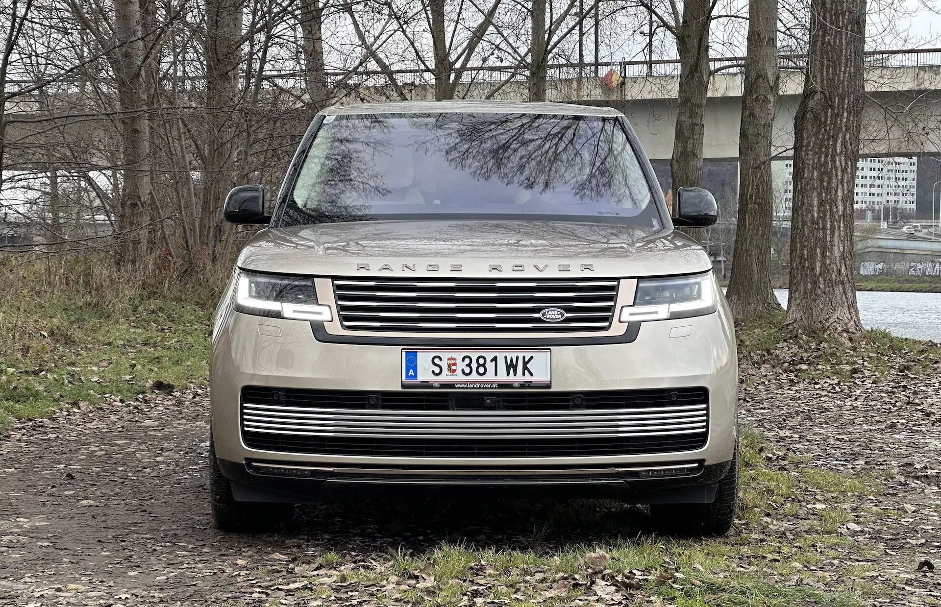 Vista frontal de un Range Rover 2021 mostrando la parrilla, faros LED, el lettering 'RANGE ROVER' en el capó y estacionado sobre una superficie no pavimentada con un entorno semi-rural