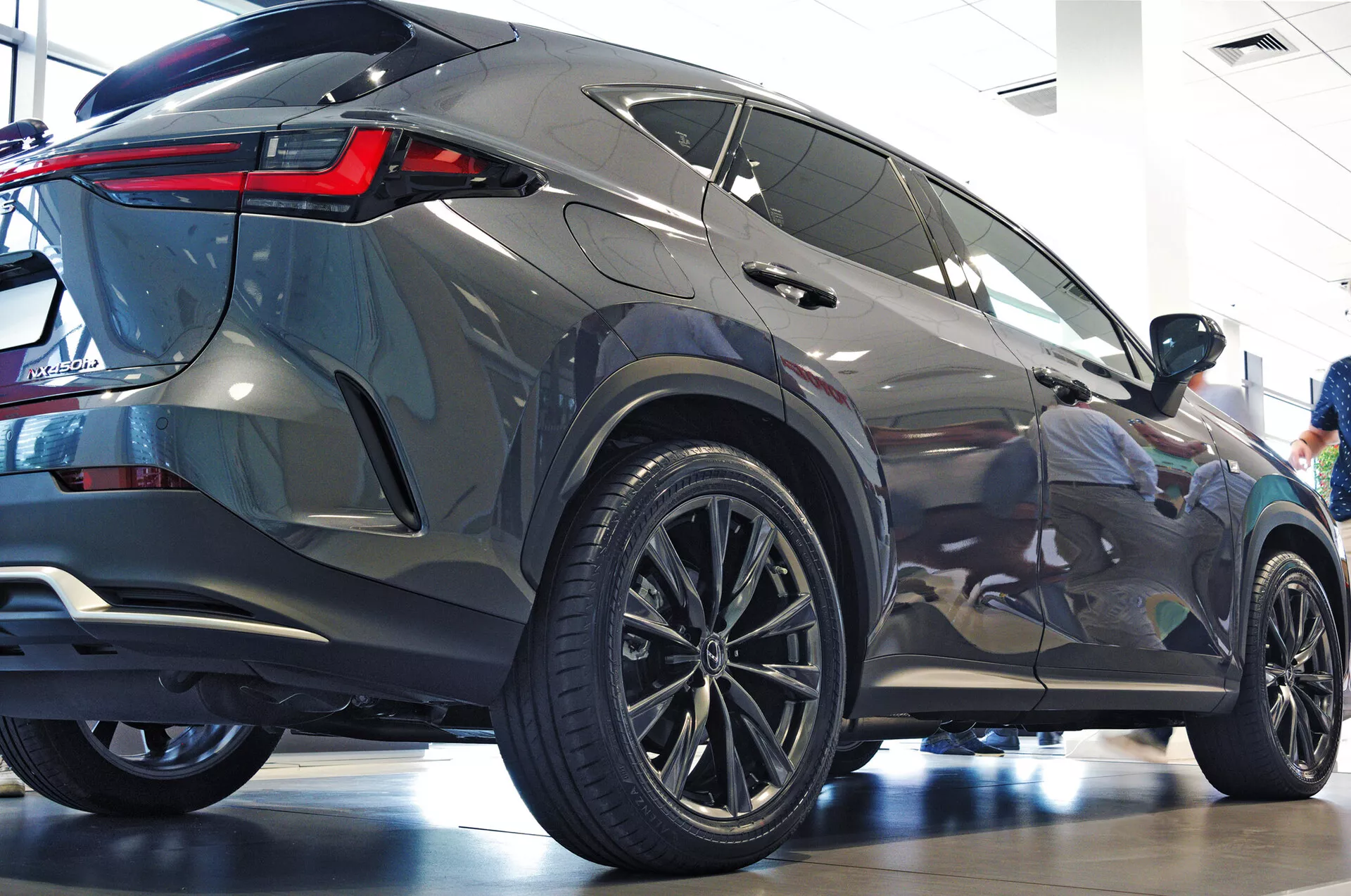 Ángulo trasero de tres cuartos del SUV Lexus NX 2021 mostrando el perfil lateral y posterior con grandes ruedas de aleación de diseño multirradio, neumáticos de perfil bajo, luces traseras LED angulares y nítidas, carrocería metálica, ventanas tintadas, alerón trasero integrado y entorno de sala de exposición pulido que enfatiza la estética moderna y las características de lujo