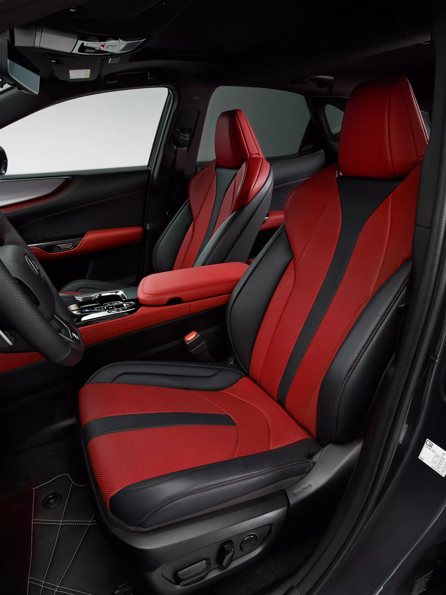 Foto del interior de un Lexus NX 2021 que muestra el área del pasajero delantero desde el ángulo del lado del conductor. La imagen destaca el asiento del pasajero con tapicería roja y detalles en negro, con un diseño deportivo y refuerzos mejorados y controles eléctricos. El panel de la puerta combina con el esquema de colores negro y rojo, cuenta con cuero, tela, un bolsillo de almacenamiento, una rejilla de altavoz y varios controles. La consola central muestra una palanca de cambios automática y un reposabrazos central con costuras rojas, reflejando el diseño lujoso y deportivo del vehículo.